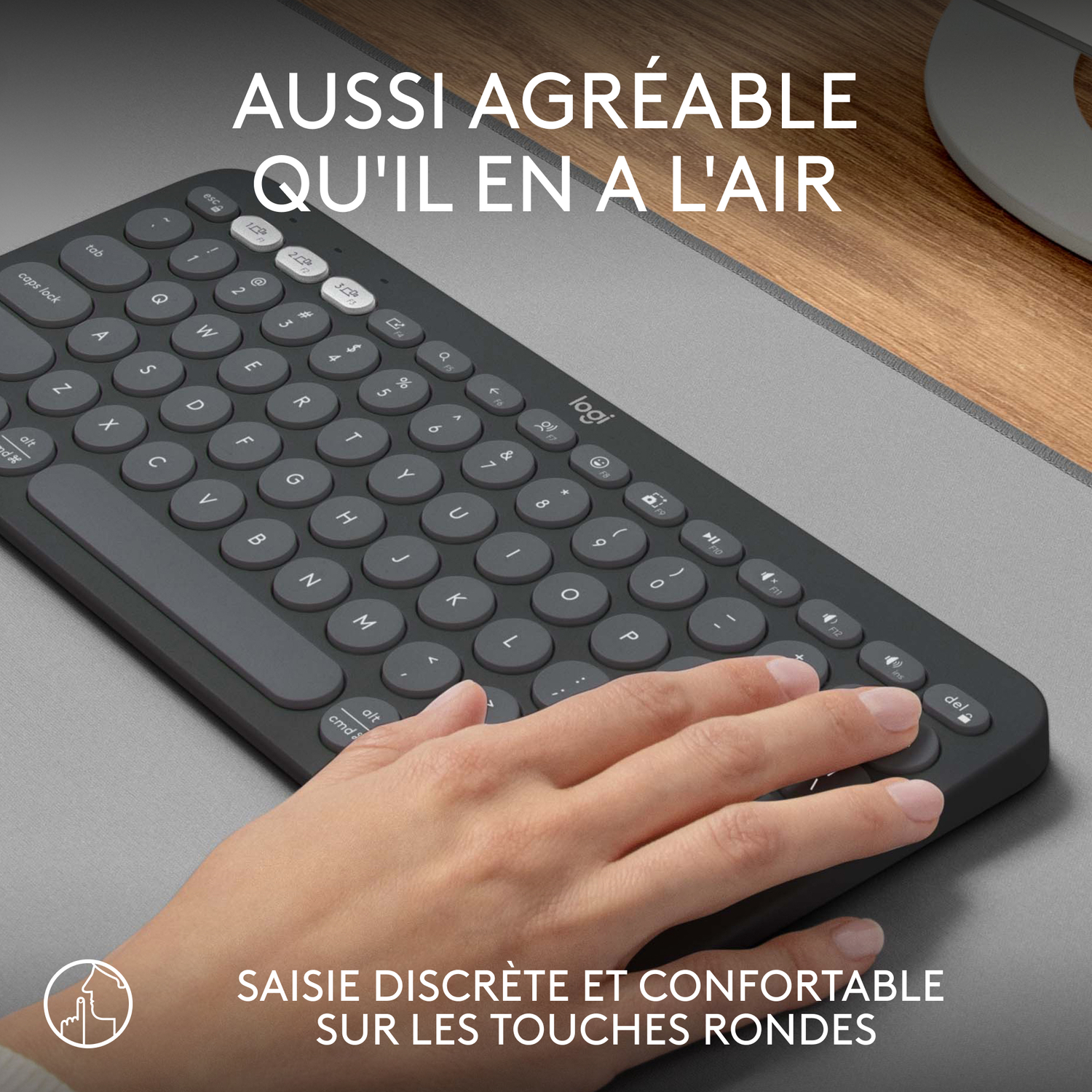 Un clavier gris avec des touches rondes. Une main repose dessus, près de la barre d'espace.