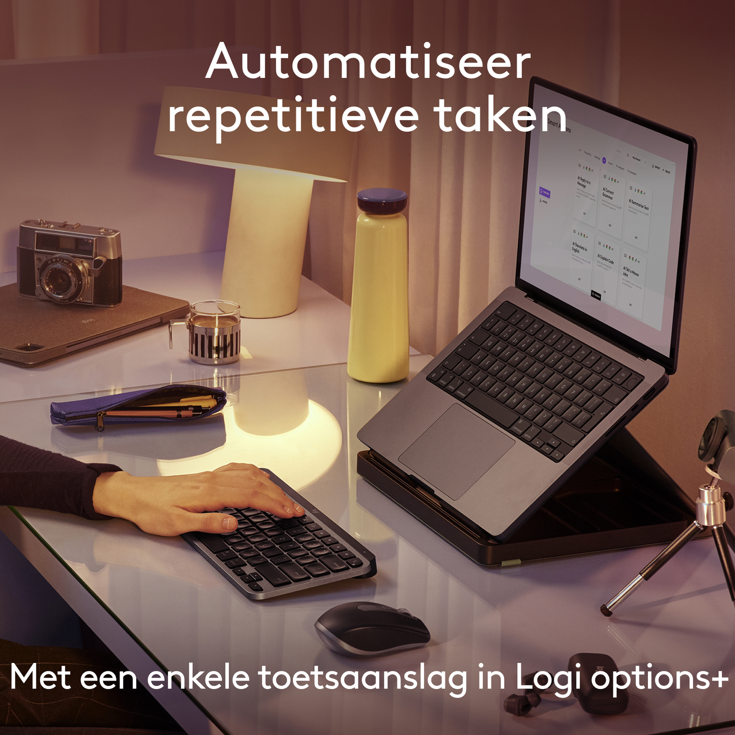 Persoon gebruikt toetsenbord met laptop, muis, lamp en fles op glazen bureau.