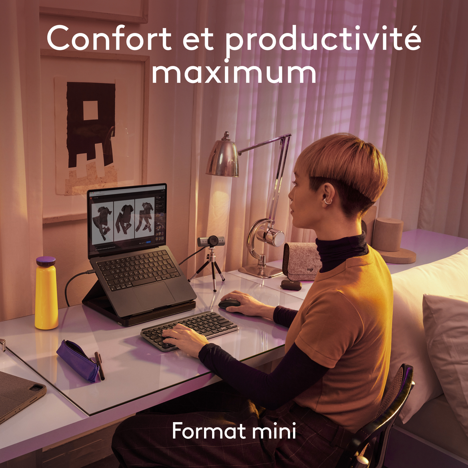 Une femme utilise un ordinateur portable et un clavier. Une bouteille jaune et une webcam sont sur le bureau.