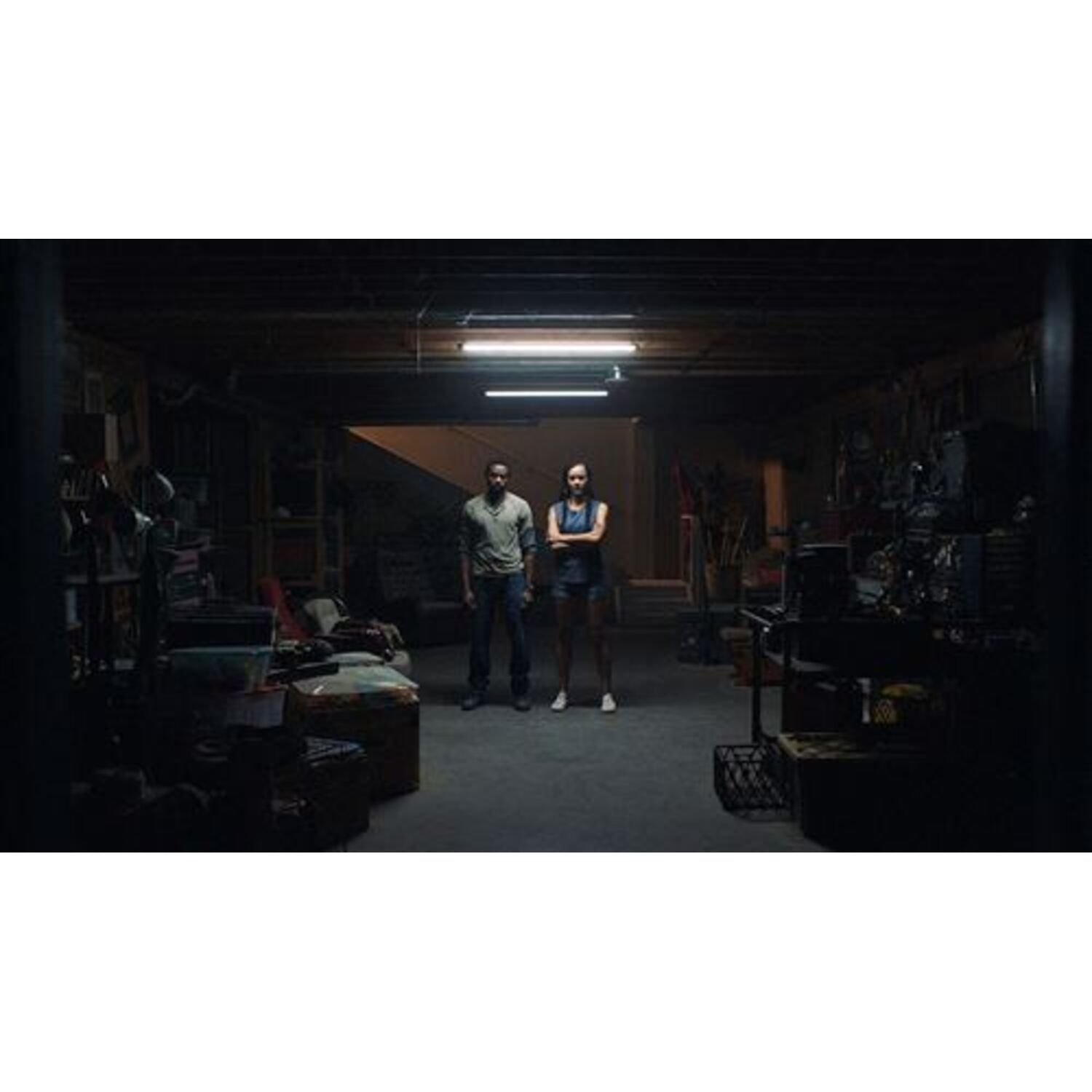 Two people stand in a dimly lit basement with various items.