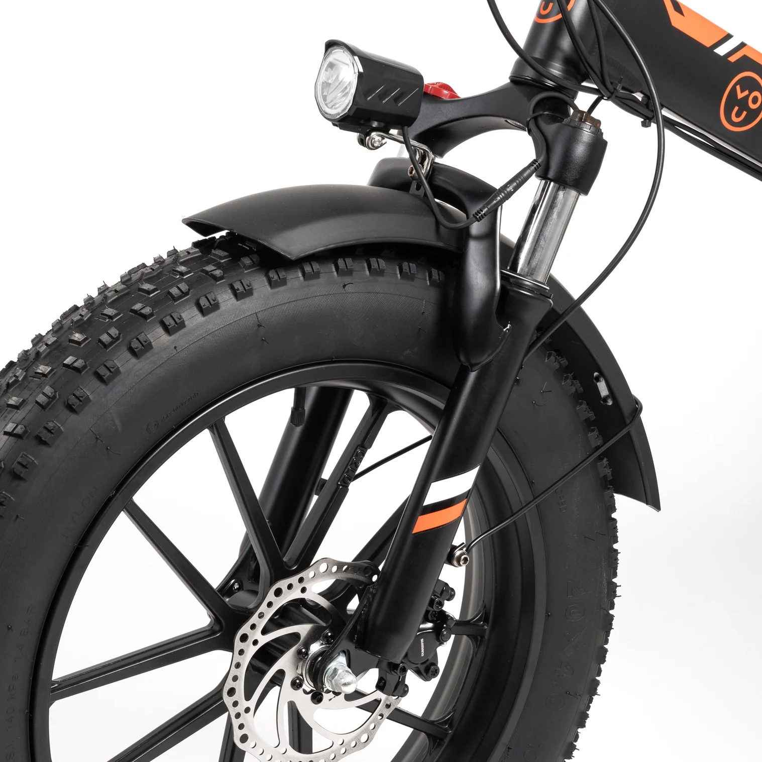 Primer plano de la parte delantera de una bicicleta eléctrica negra. Neumático negro, guardabarros, luz delantera y freno de disco sobre fondo blanco.