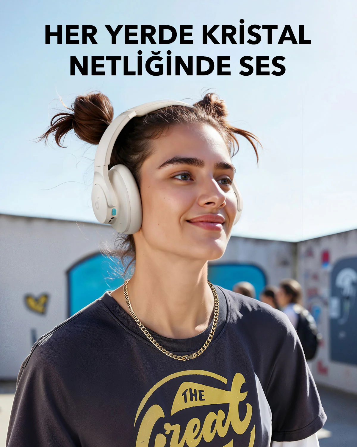 Beyaz kulaklık, altın zincir ve siyah tişört giyen kadın. Arka planda grafitili duvar ve mavi gökyüzü. Üstte Türkçe metin.