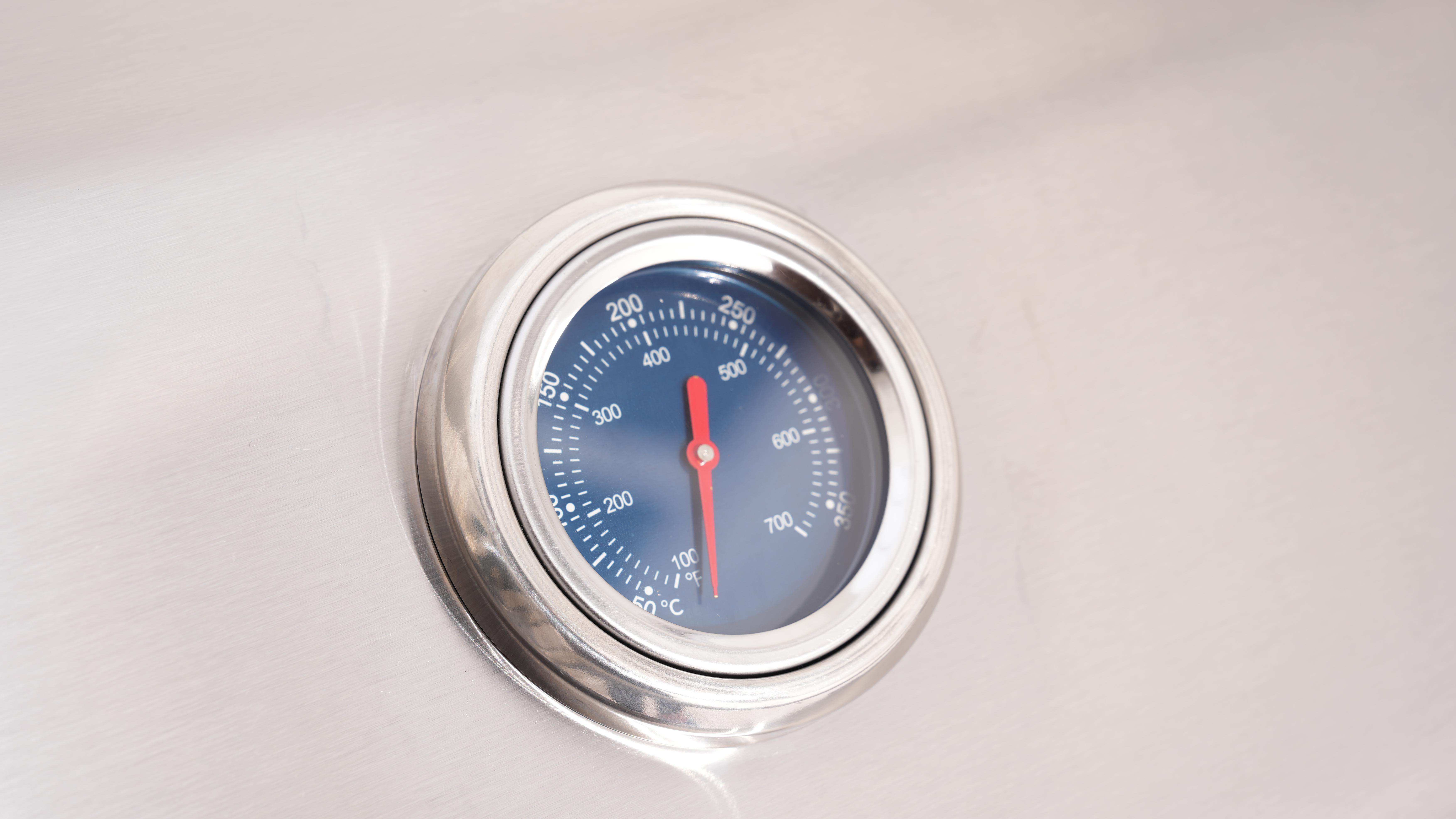 Nahaufnahme eines Edelstahl-Grillthermometers. Es hat ein blaues Zifferblatt und eine rote Nadel, die die Temperatur anzeigt.