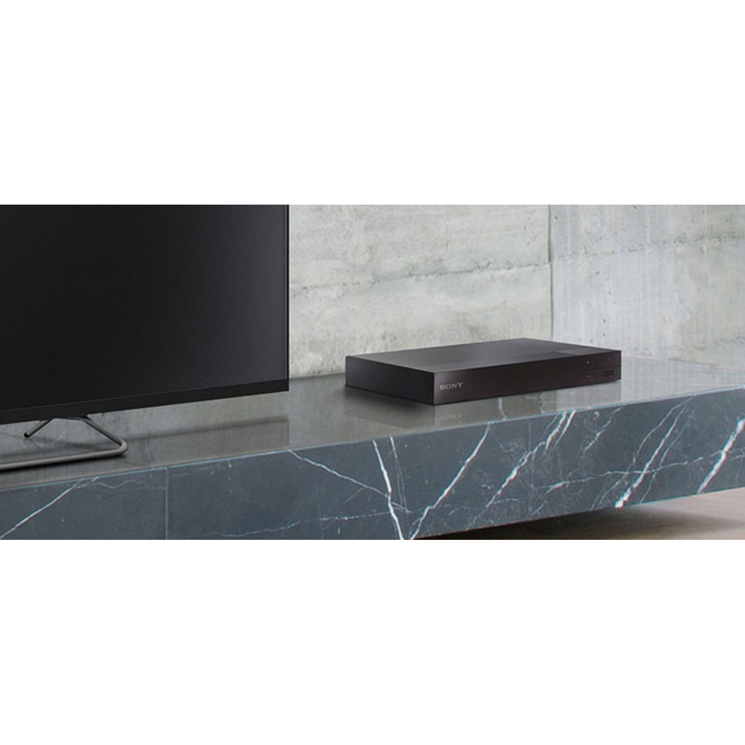 A black Sony device on a marble surface, next to a TV screen. The room is minimalist.