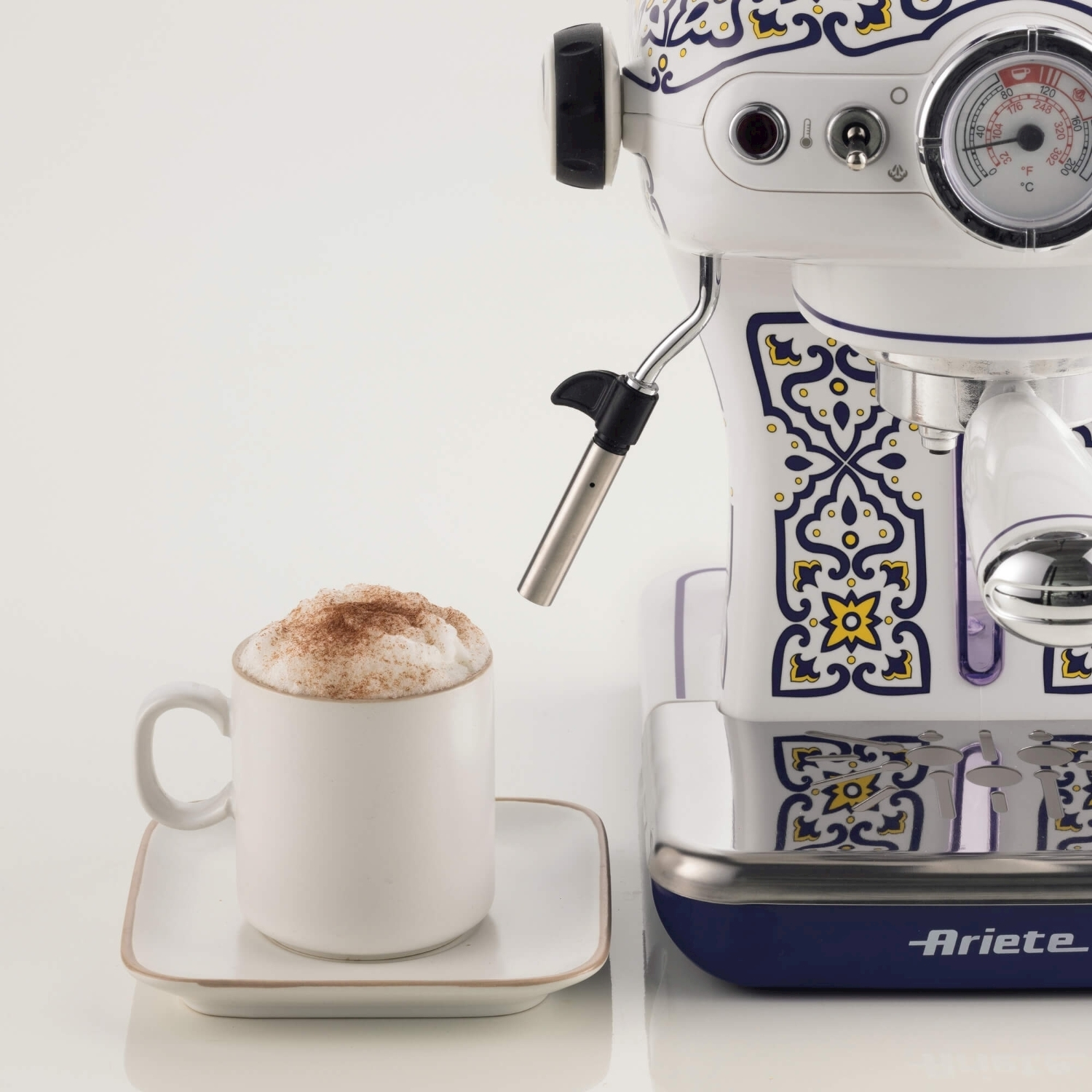 Una macchina per espresso bianca e blu con una tazza di cappuccino su un piattino. La macchina ha un motivo floreale.