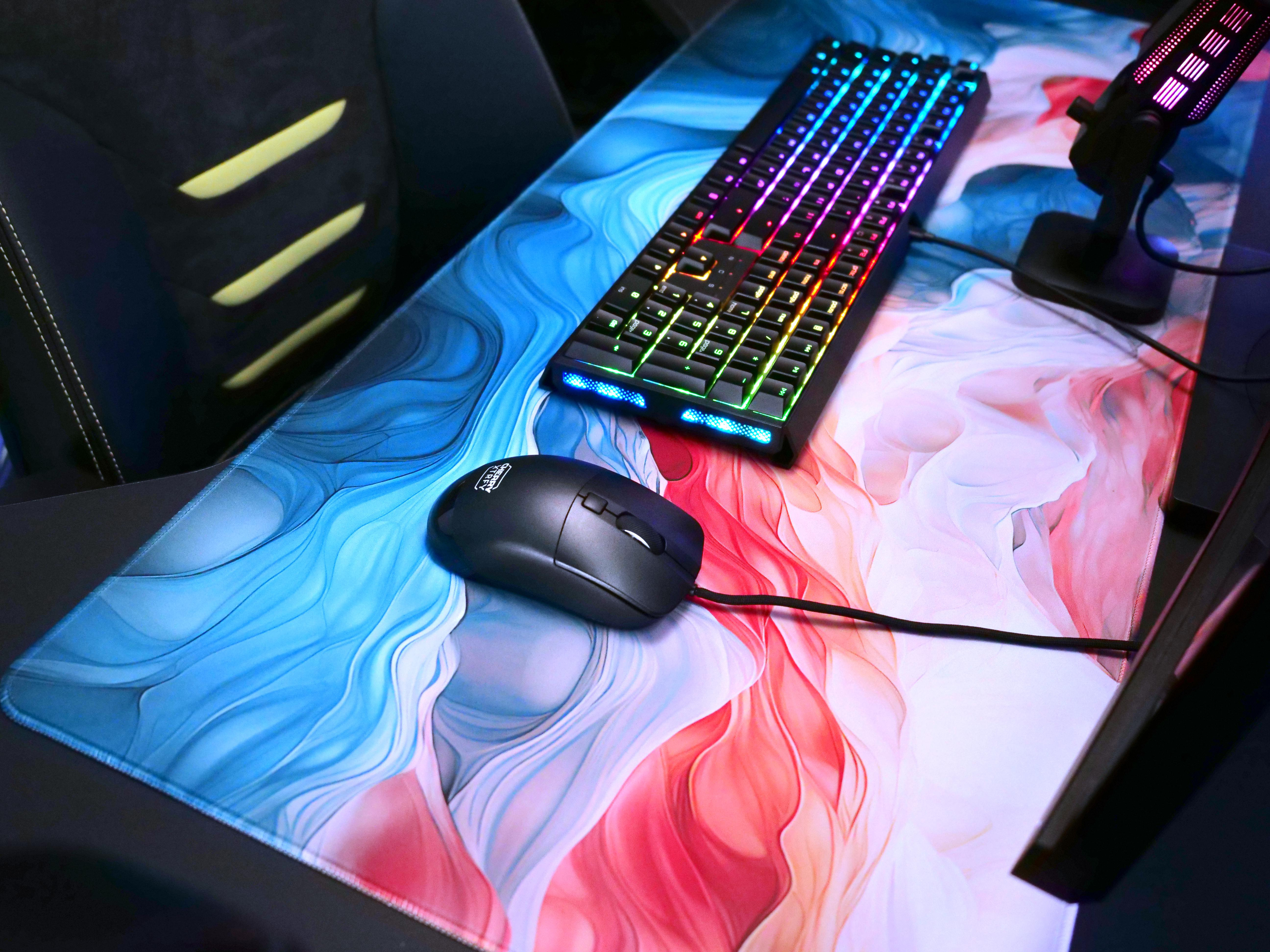 Ein Gaming-Setup mit Tastatur, Maus und buntem Mauspad auf dunkler Oberfläche.