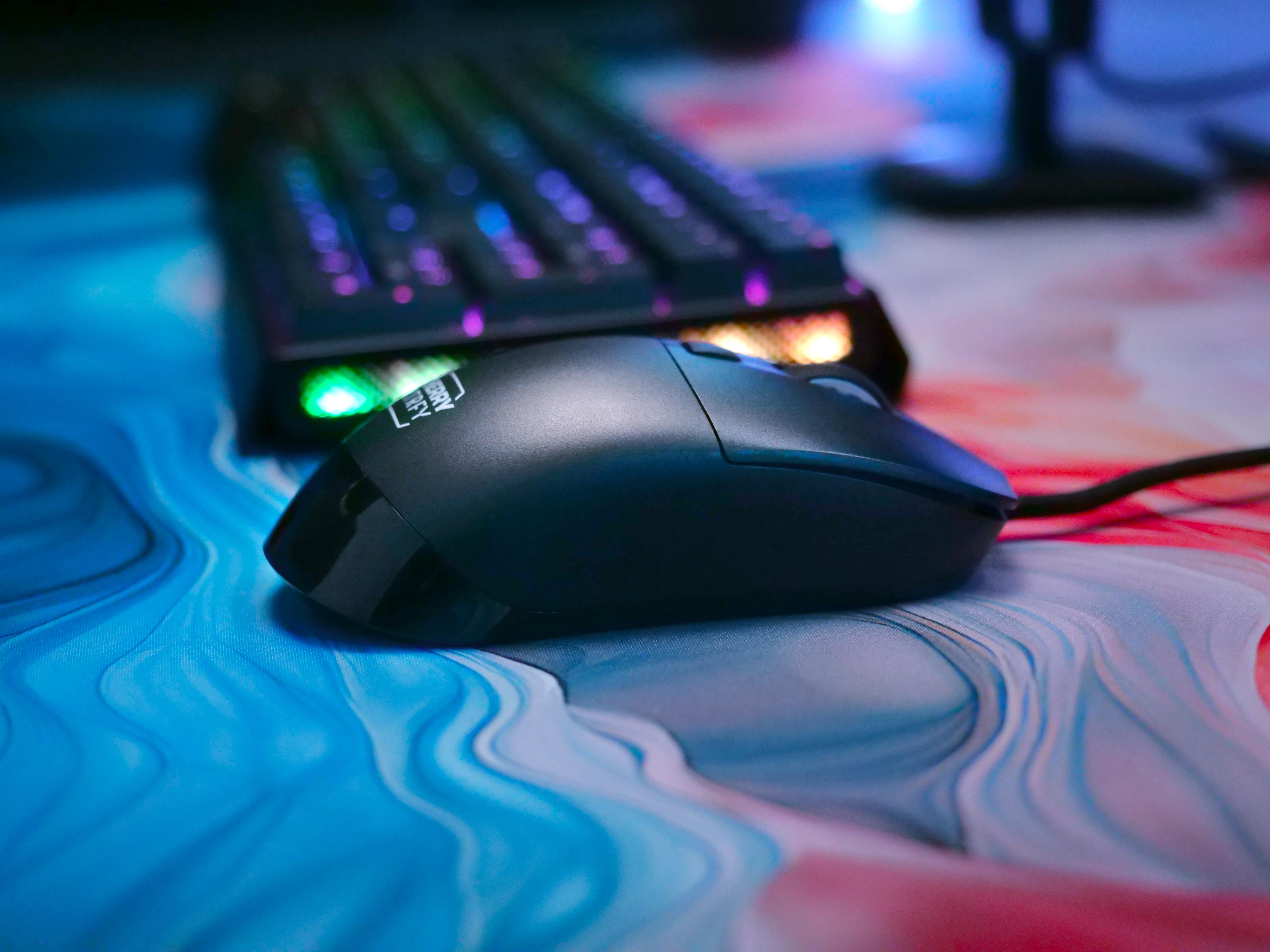 Schwarze Computermaus neben einer Tastatur auf einem Gaming-Mauspad mit blauen und roten Farben.