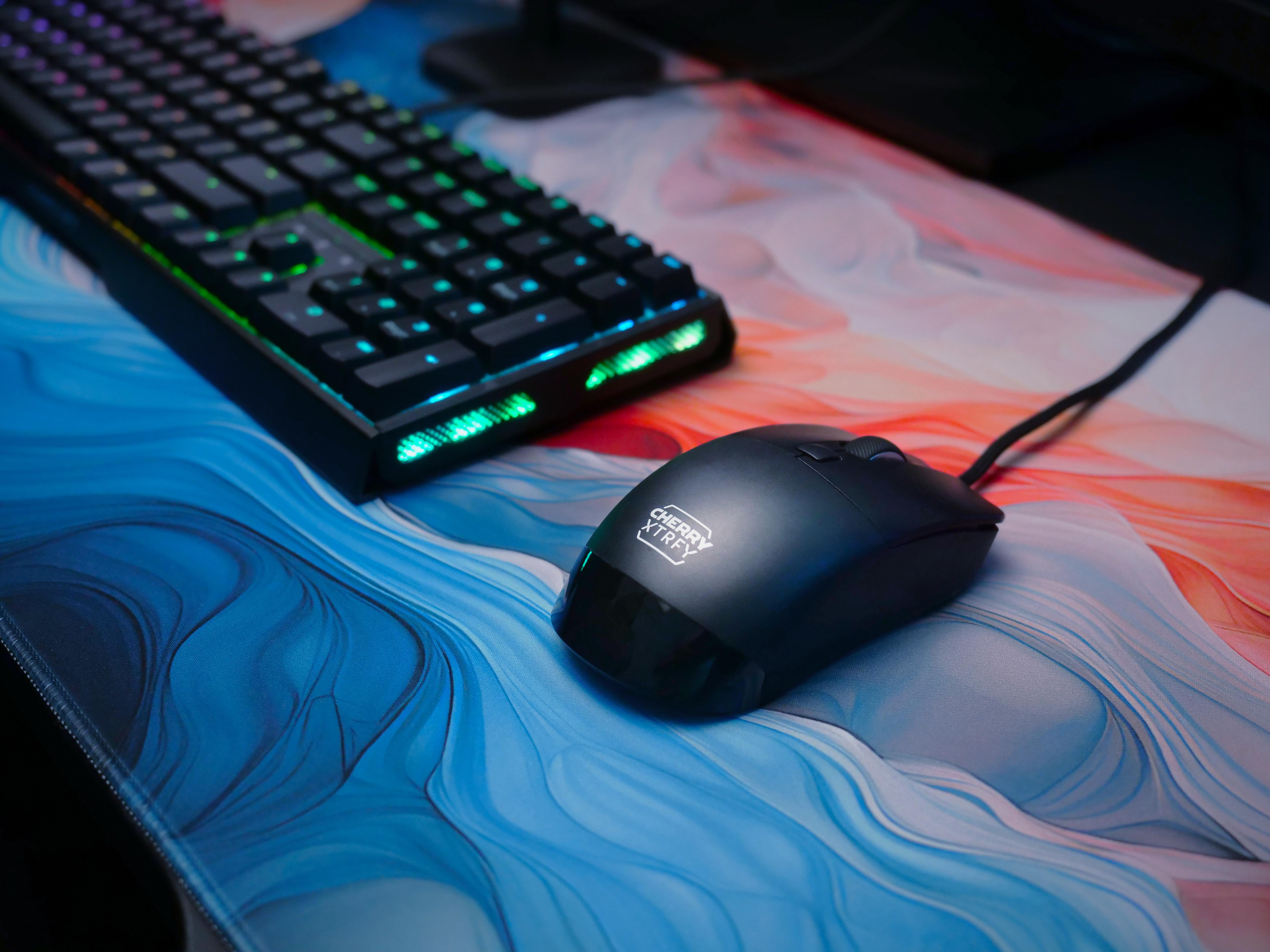 Schwarze Maus und Tastatur auf einem blau-rot gemusterten Mousepad.
