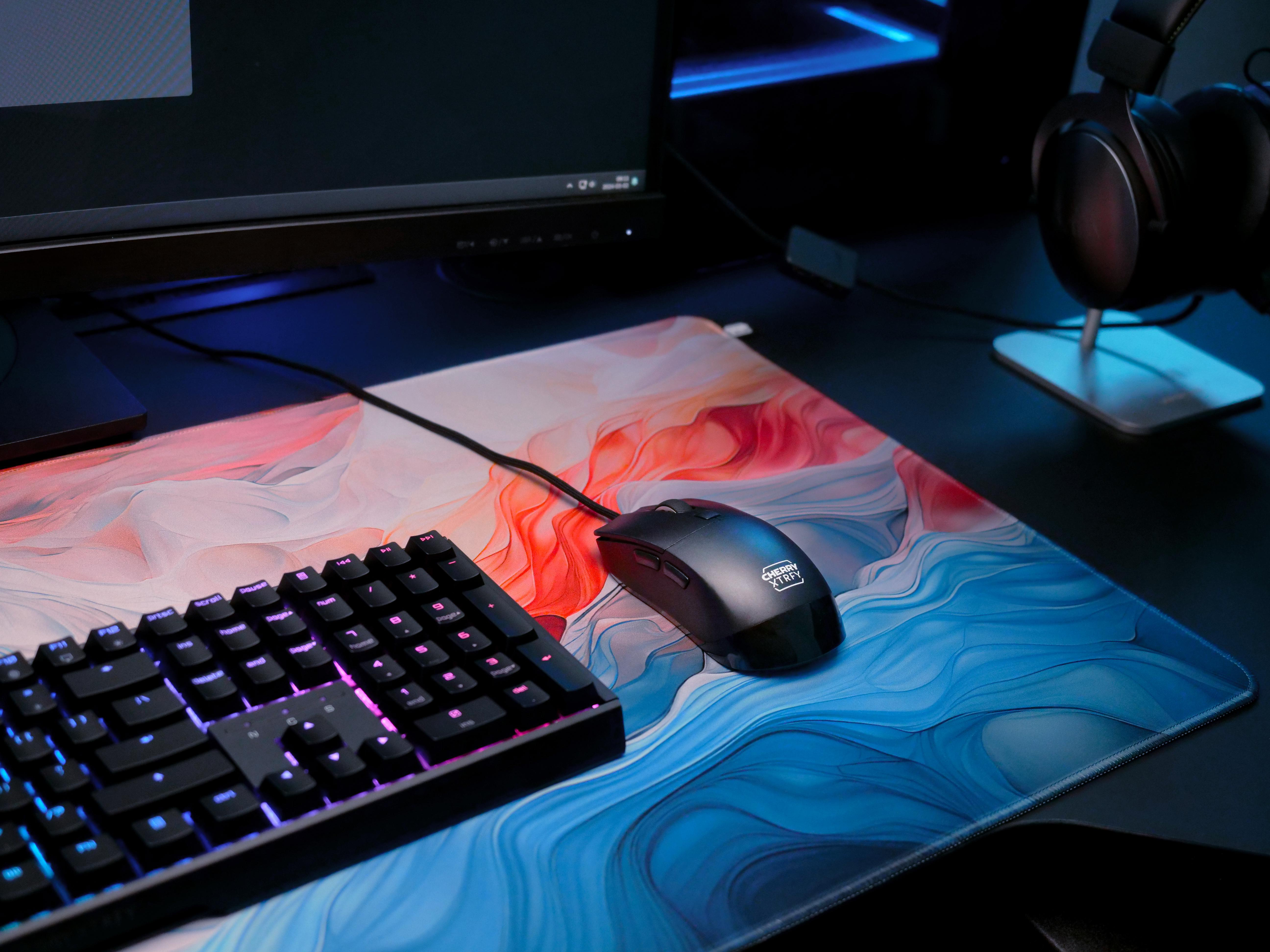 Gaming-Setup mit Tastatur, Maus, Mauspad und Monitor, alles dunkel gehalten.