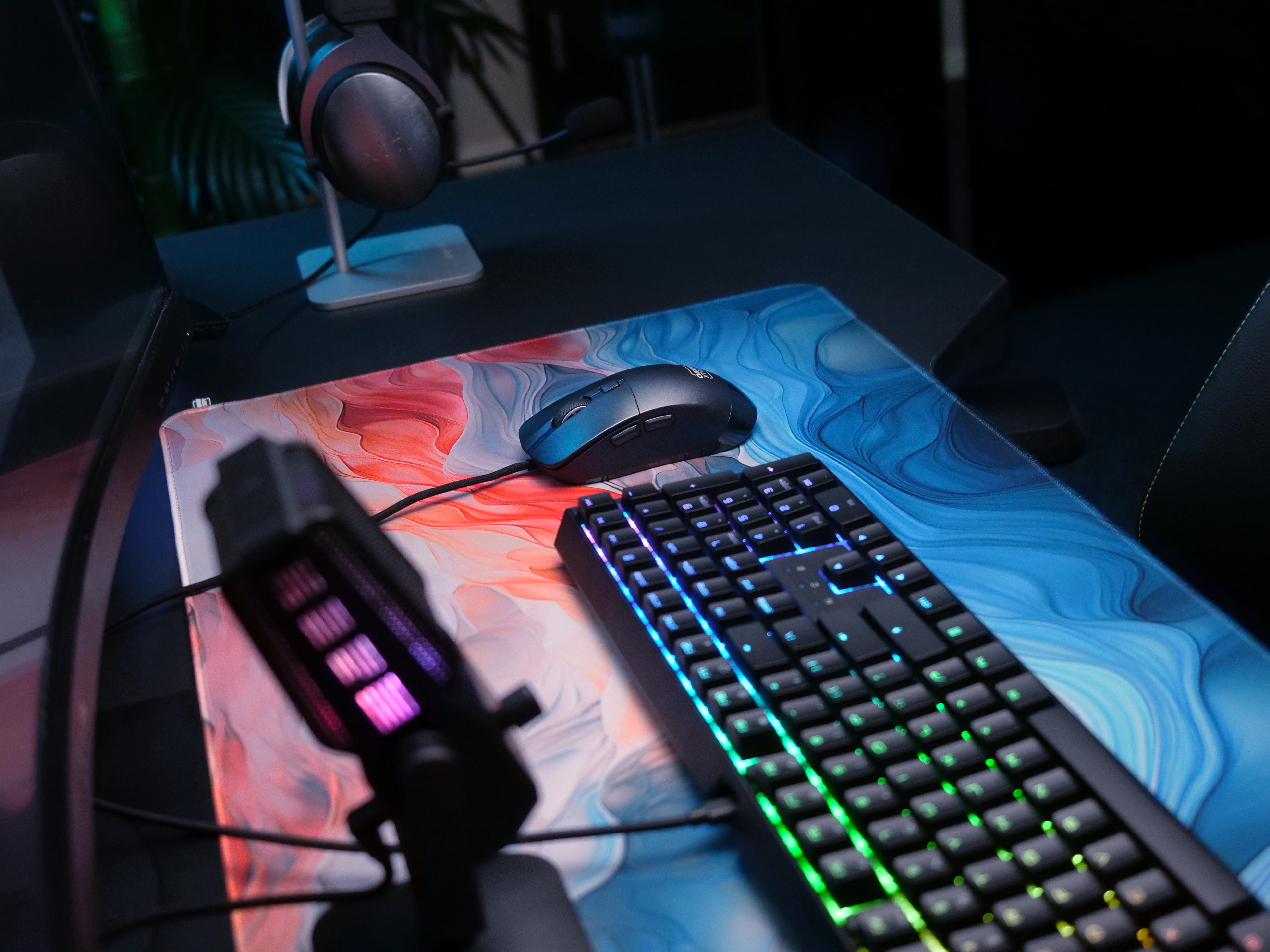 Gaming-Setup mit Tastatur, Maus, Mikrofon und Mauspad mit abstrakter Kunst.