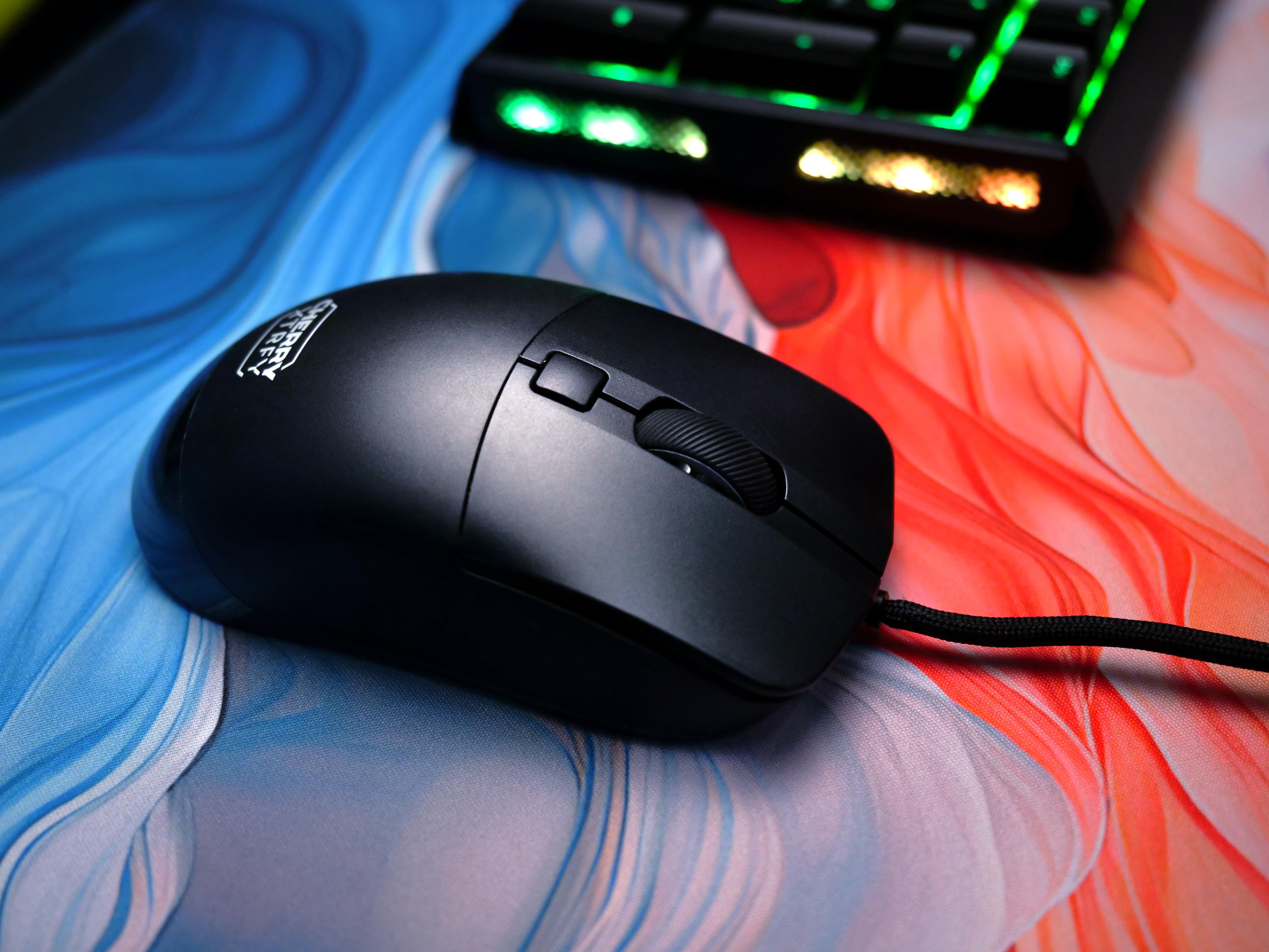 Eine schwarze Computermaus auf einem farbenfrohen Gaming-Mauspad, Tastatur im Hintergrund.