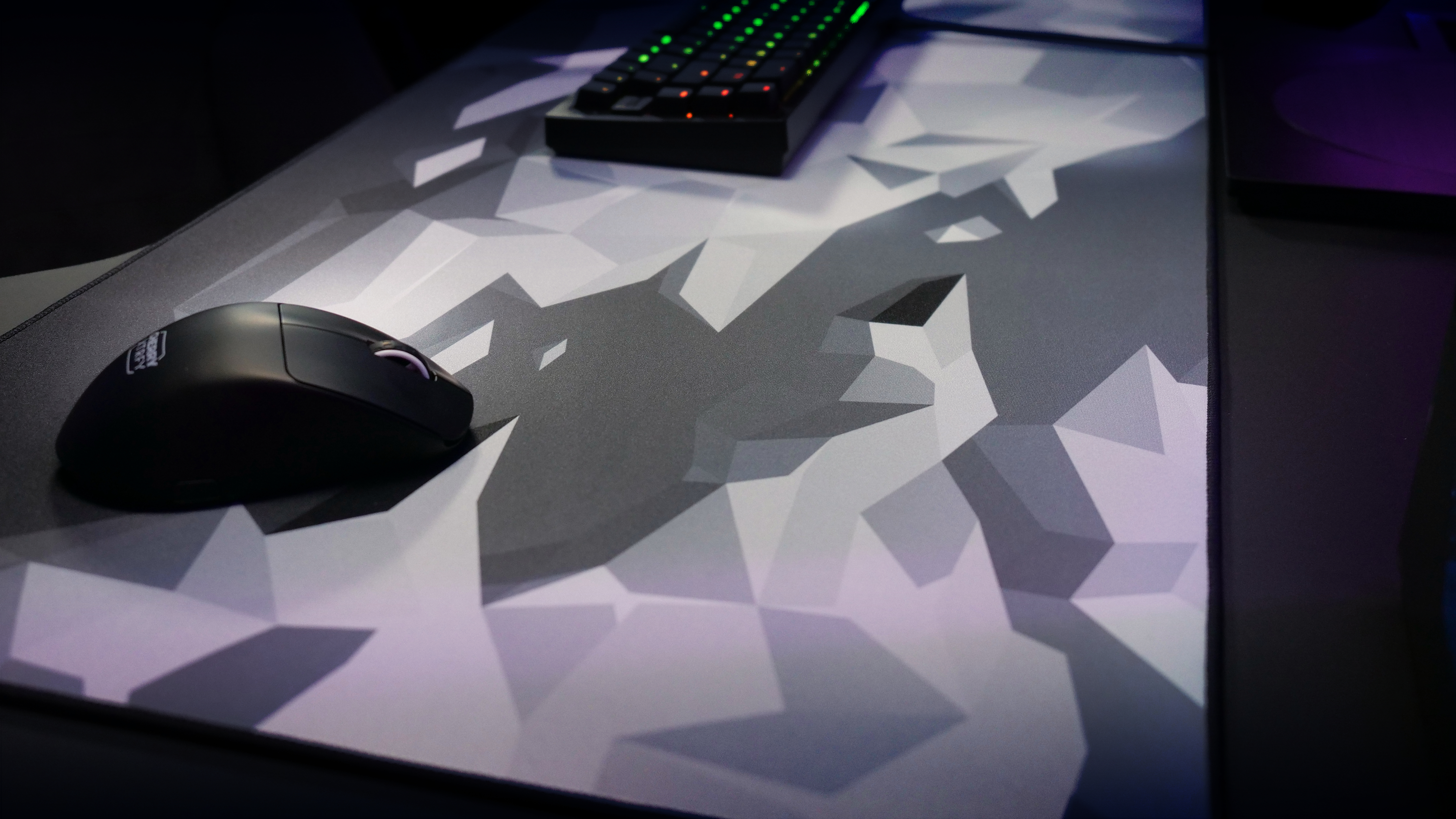 Gaming-Setup mit Tastatur und Maus auf gemusterter Matte. Verschwommener Hintergrund mit Tastatur.