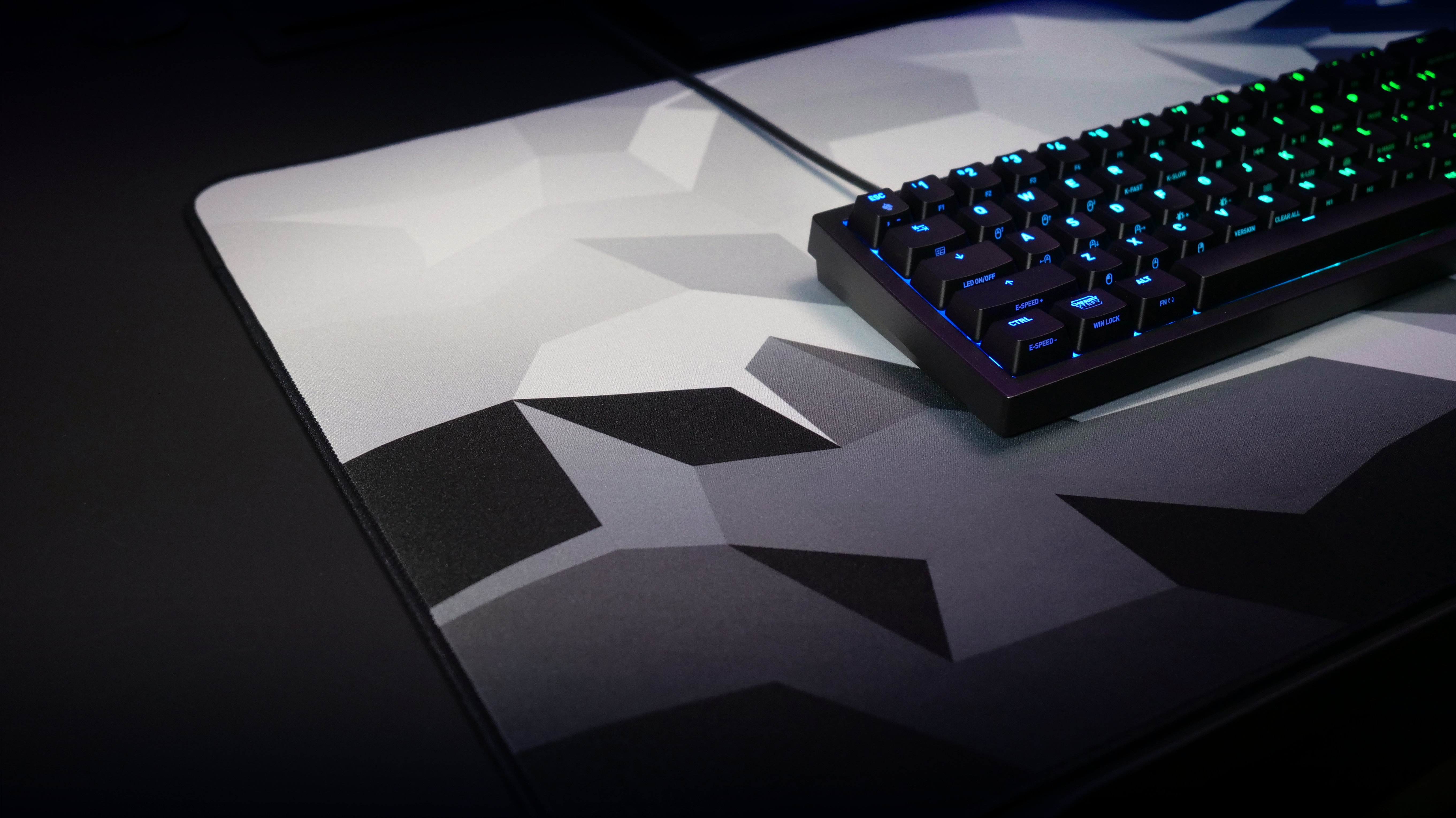 Eine schwarze Tastatur auf einem Gaming-Mauspad mit geometrischem Muster und schwarzem Schreibtisch.
