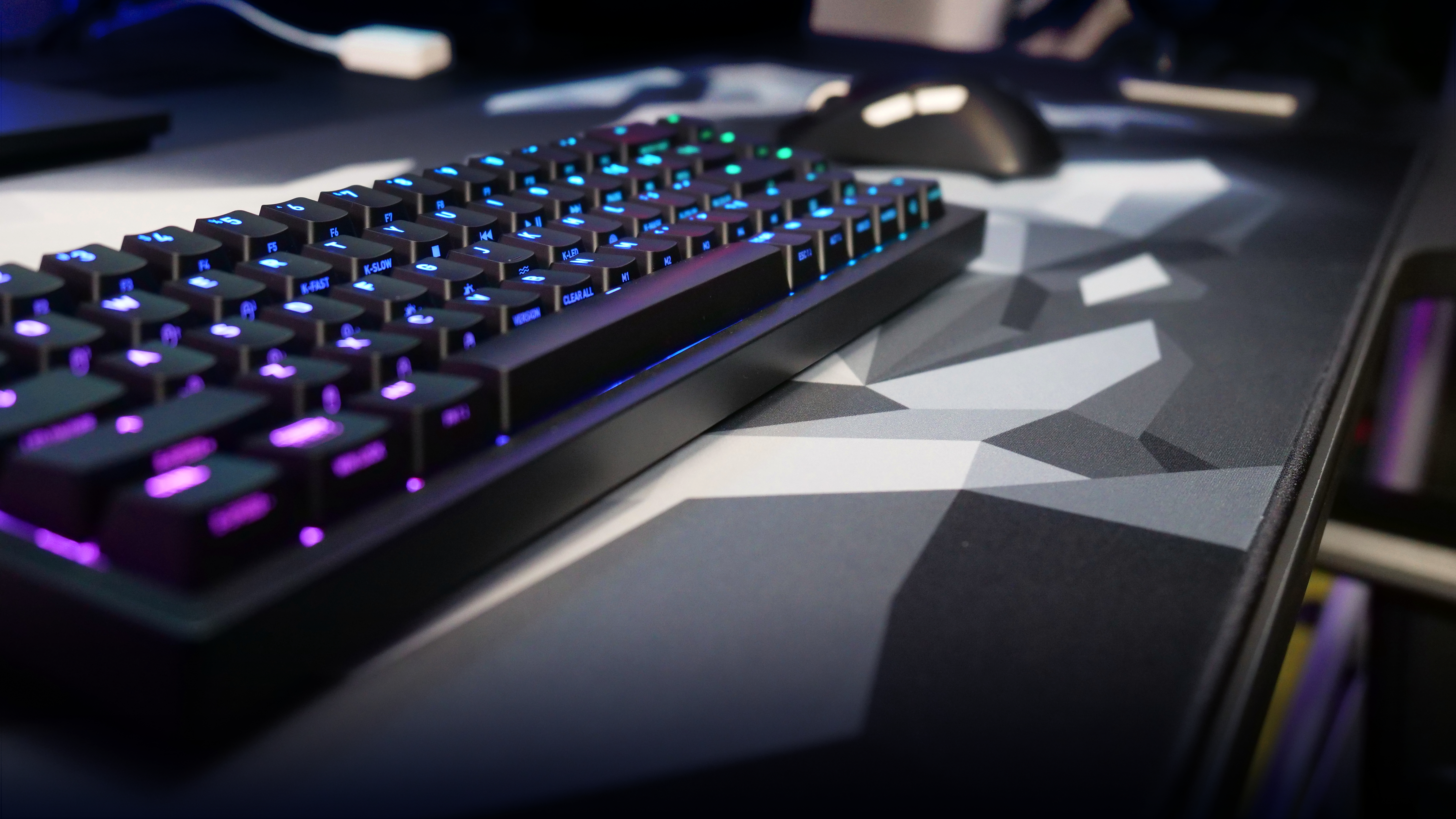Schwarze mechanische Tastatur mit beleuchteten Tasten, auf einer gemusterten Schreibtischunterlage.