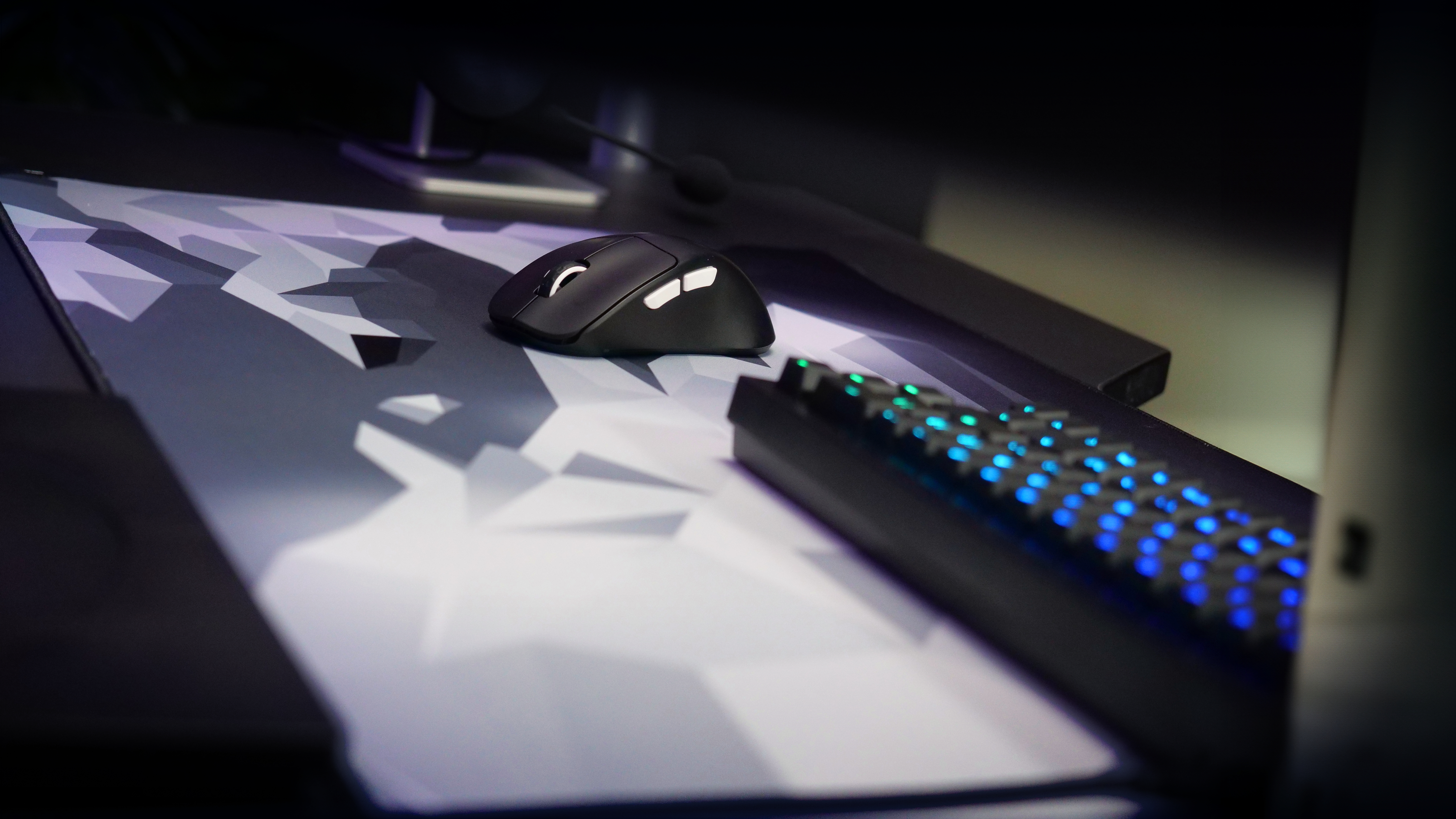 Schwarze Maus auf gemustertem Mauspad, Tastatur und Monitor im Hintergrund.