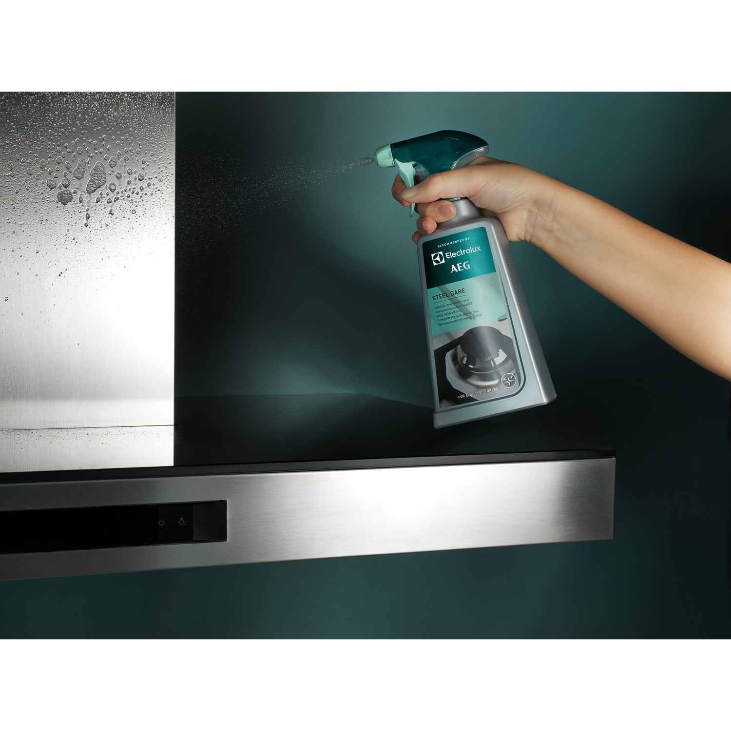 Mano che spruzza detergente su cappa in acciaio inox. Prodotto a marchio AEG.