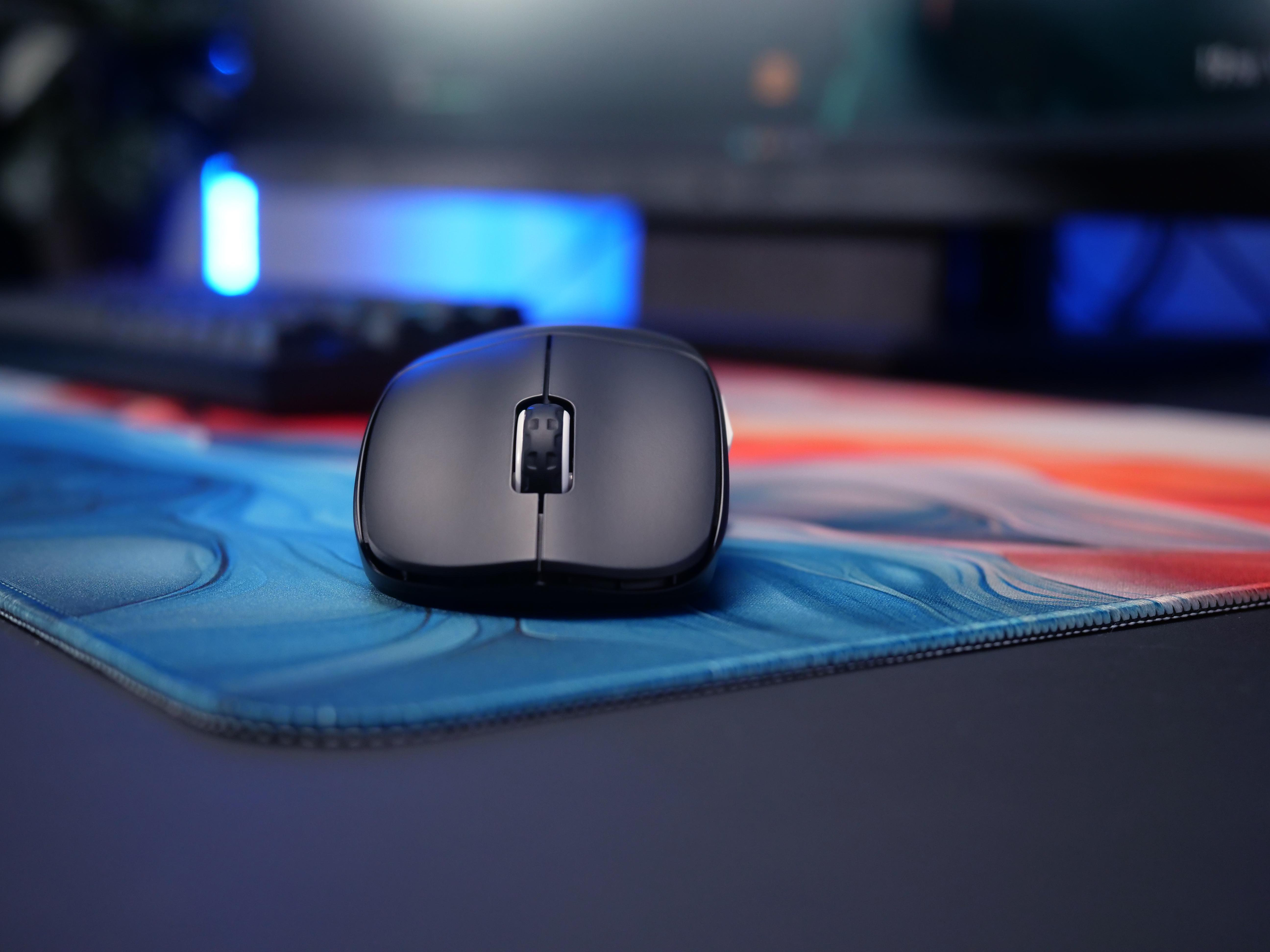 Eine schwarze, glänzende Computermaus liegt auf einem blau-rot gemusterten Mauspad.