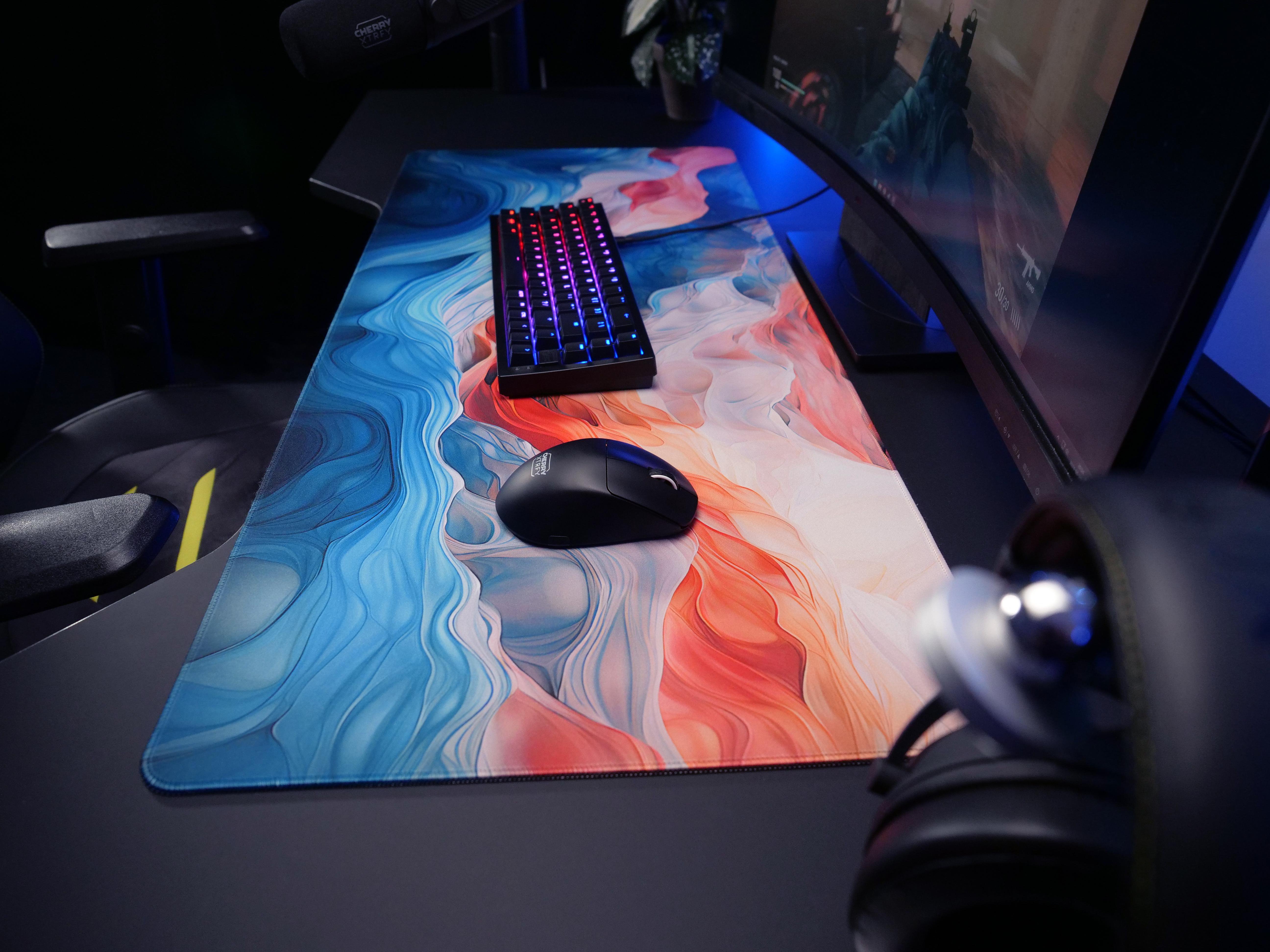 Gaming-Setup mit Tastatur, Maus und farbenfrohem Mauspad auf einem schwarzen Schreibtisch.