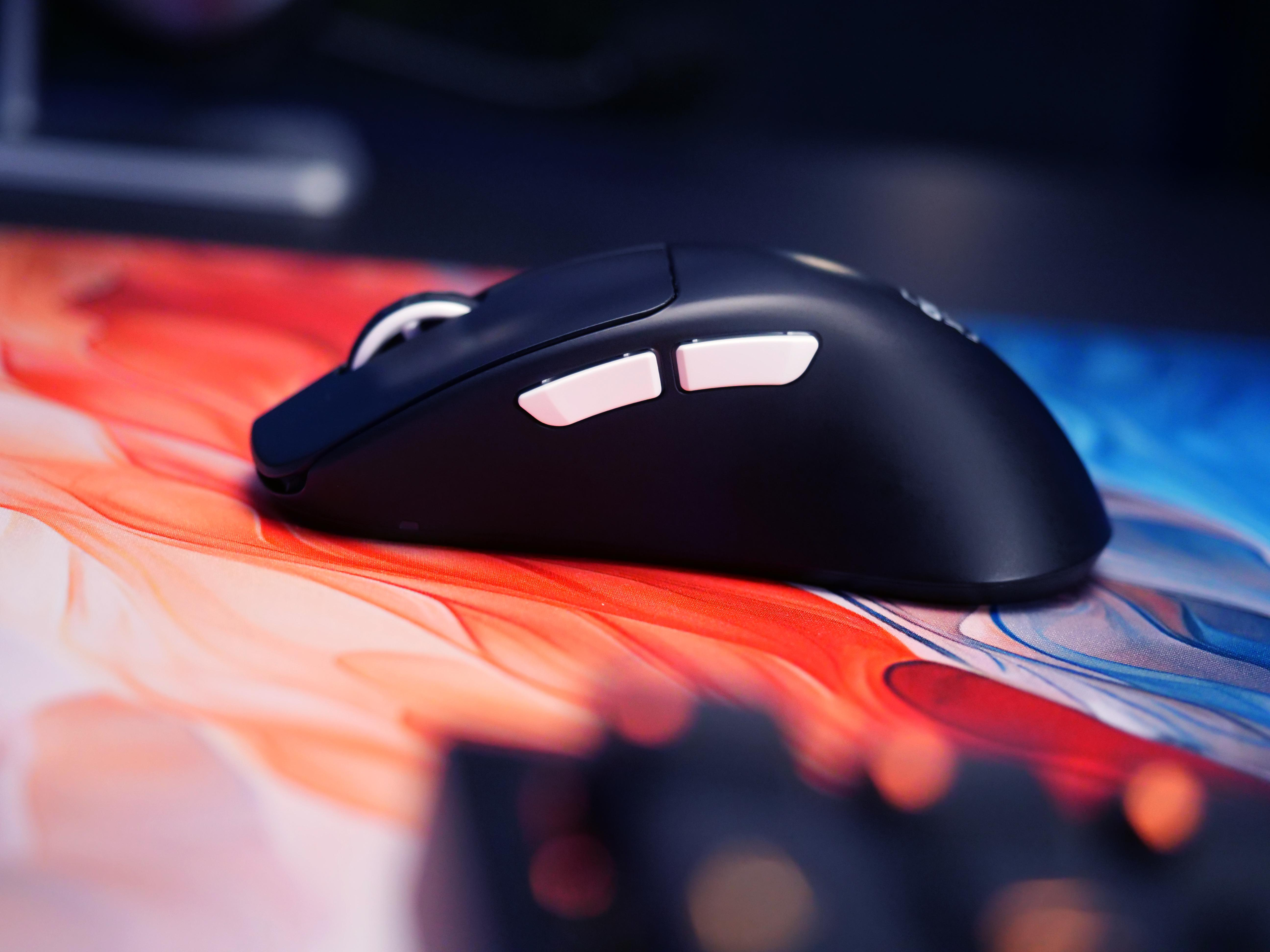 Eine schwarze Gaming-Maus auf einem farbenfrohen Mauspapier. Die Maus hat weiße Tasten.