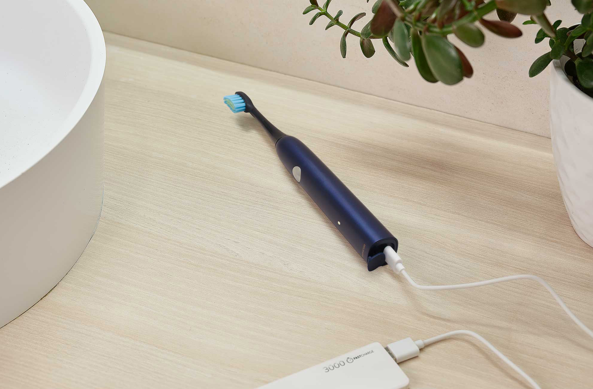 Elektromos fogkefe töltése fehér power bankkal világos fa felületen.