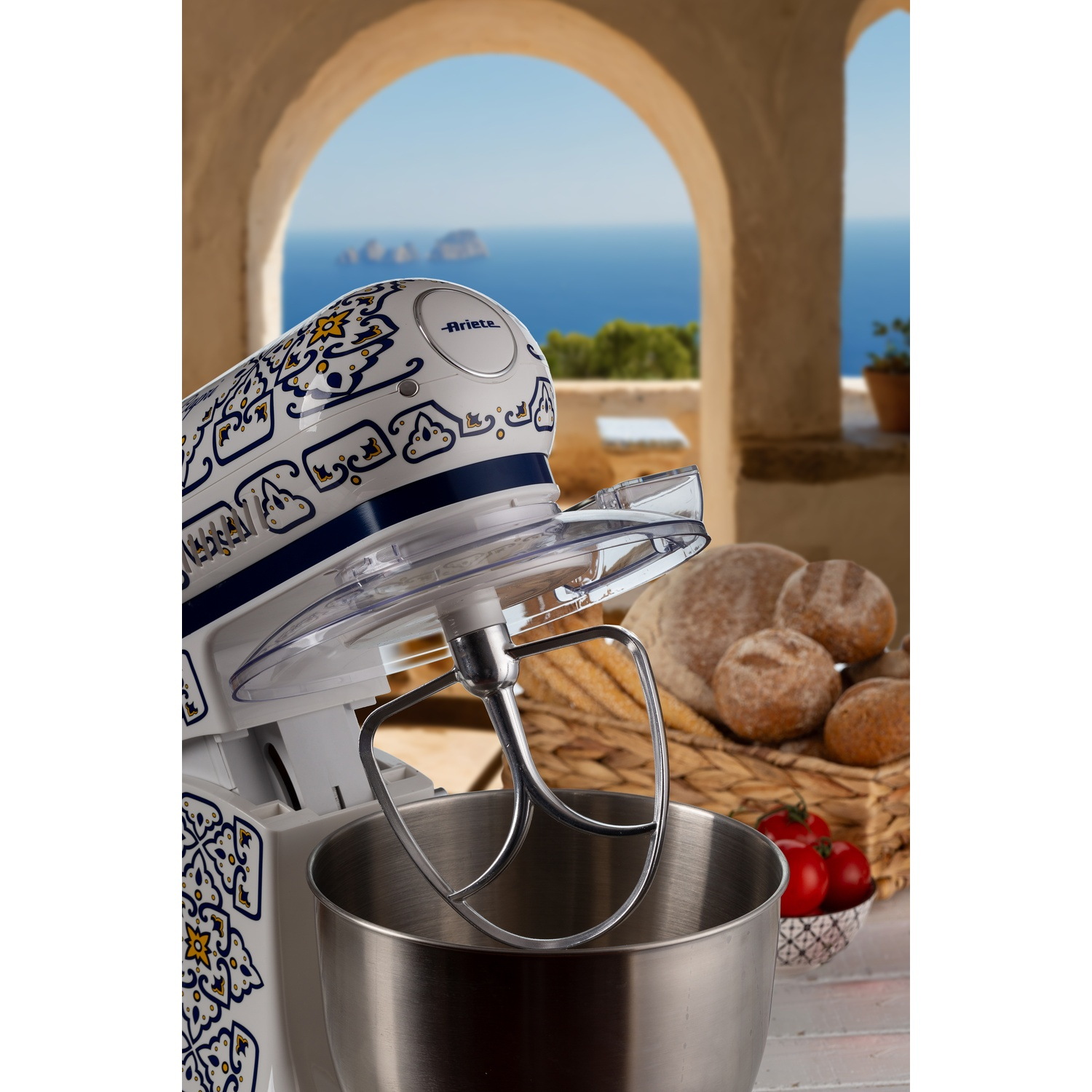 Un mixer da cucina bianco e blu con una ciotola aperta. Pane e paesaggio visibili sullo sfondo.