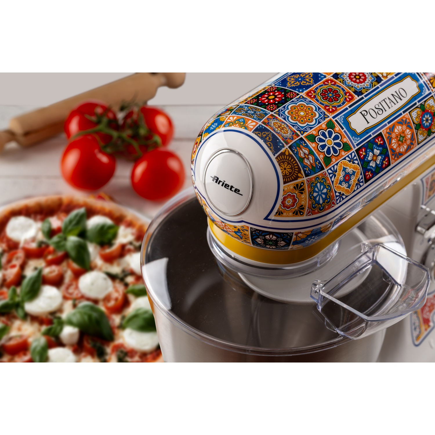 Mixer da cucina con motivo colorato. Pomodori e pizza visibili sullo sfondo.