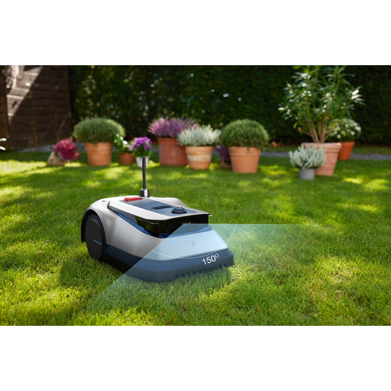 Een robotmaaier op een groen gazon met potplanten op de achtergrond.
