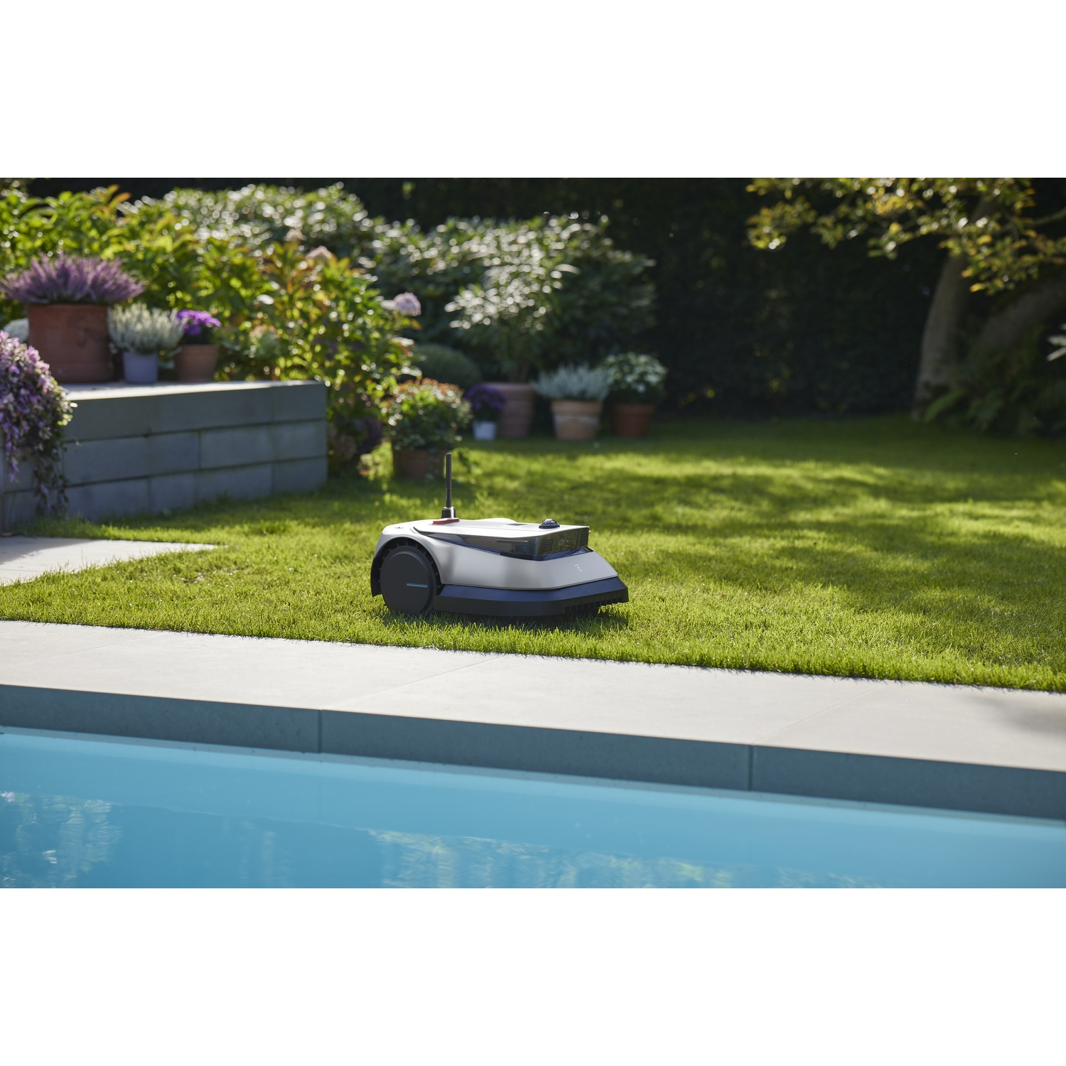 Robotmaaier op een gazon, met een zwembad op de voorgrond en tuin.