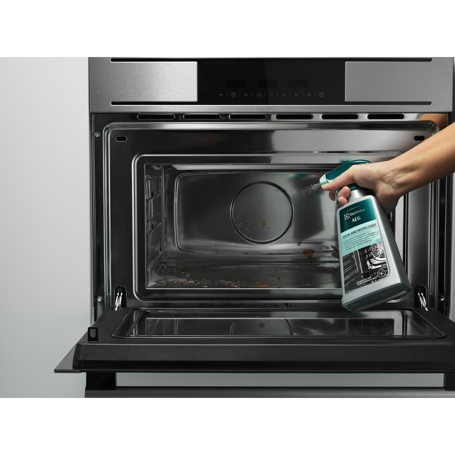 Una persona che spruzza un detergente per forno all'interno di un forno pulito.