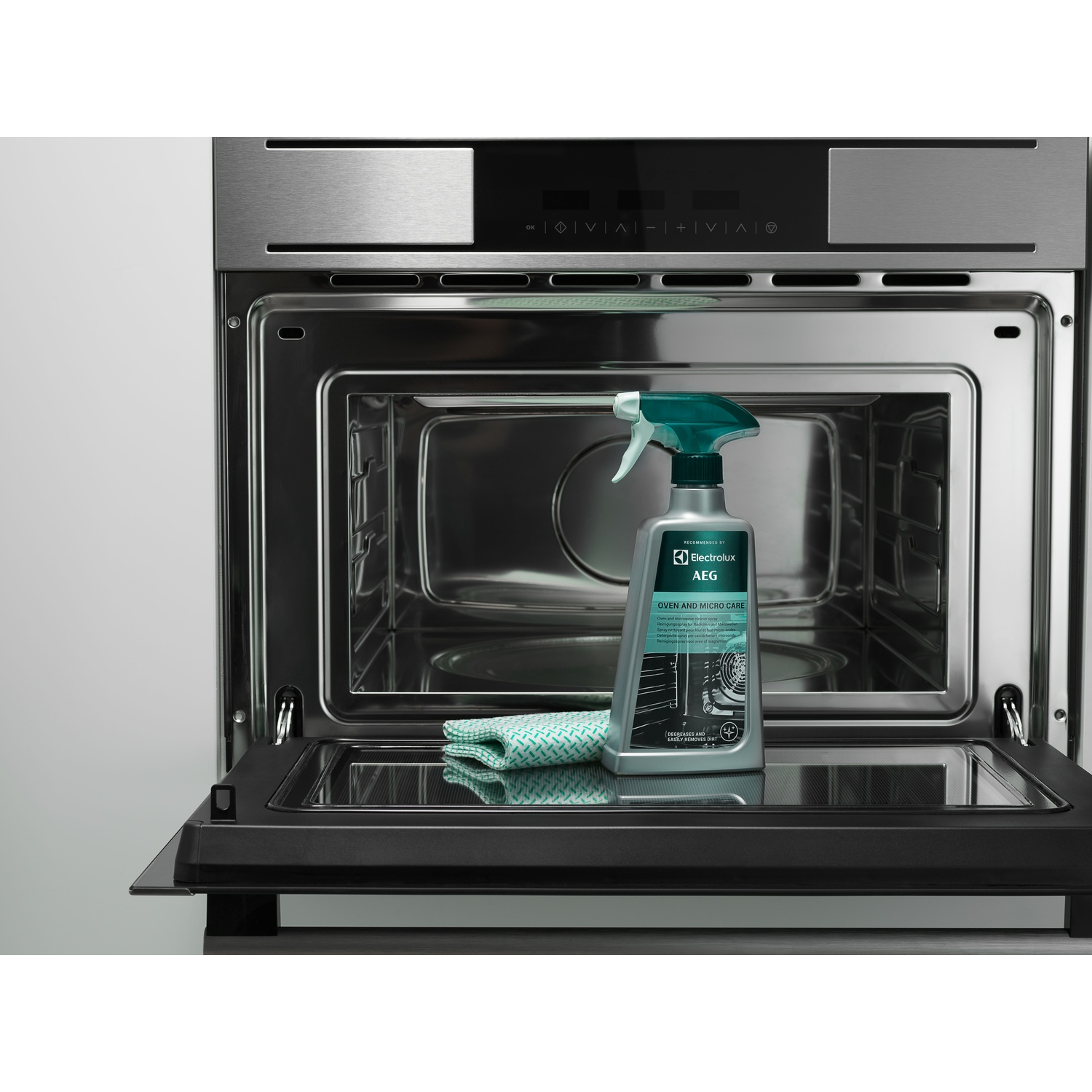 Forno a microonde aperto con spray pulente e panno all'interno. Interno argentato.