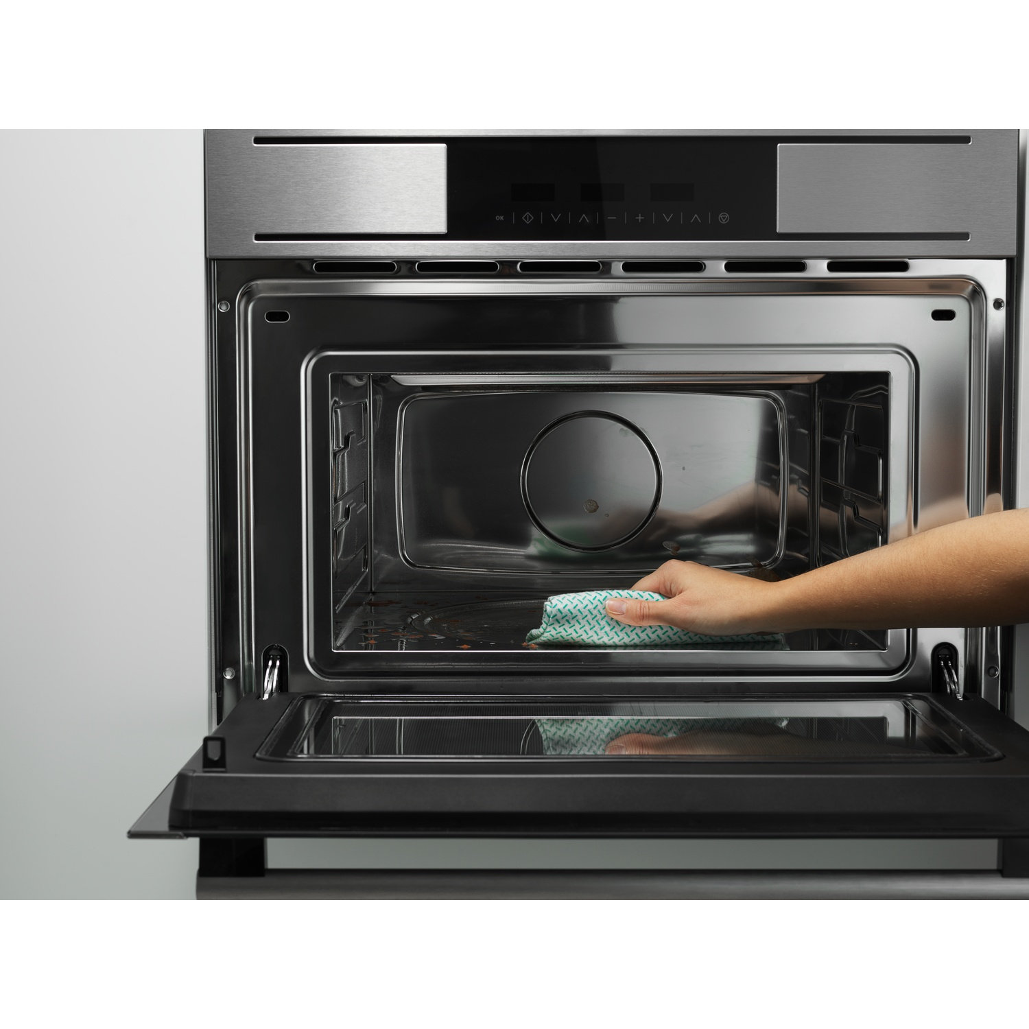 Una mano pulisce l'interno di un forno. La porta del forno è aperta e si usa un panno.