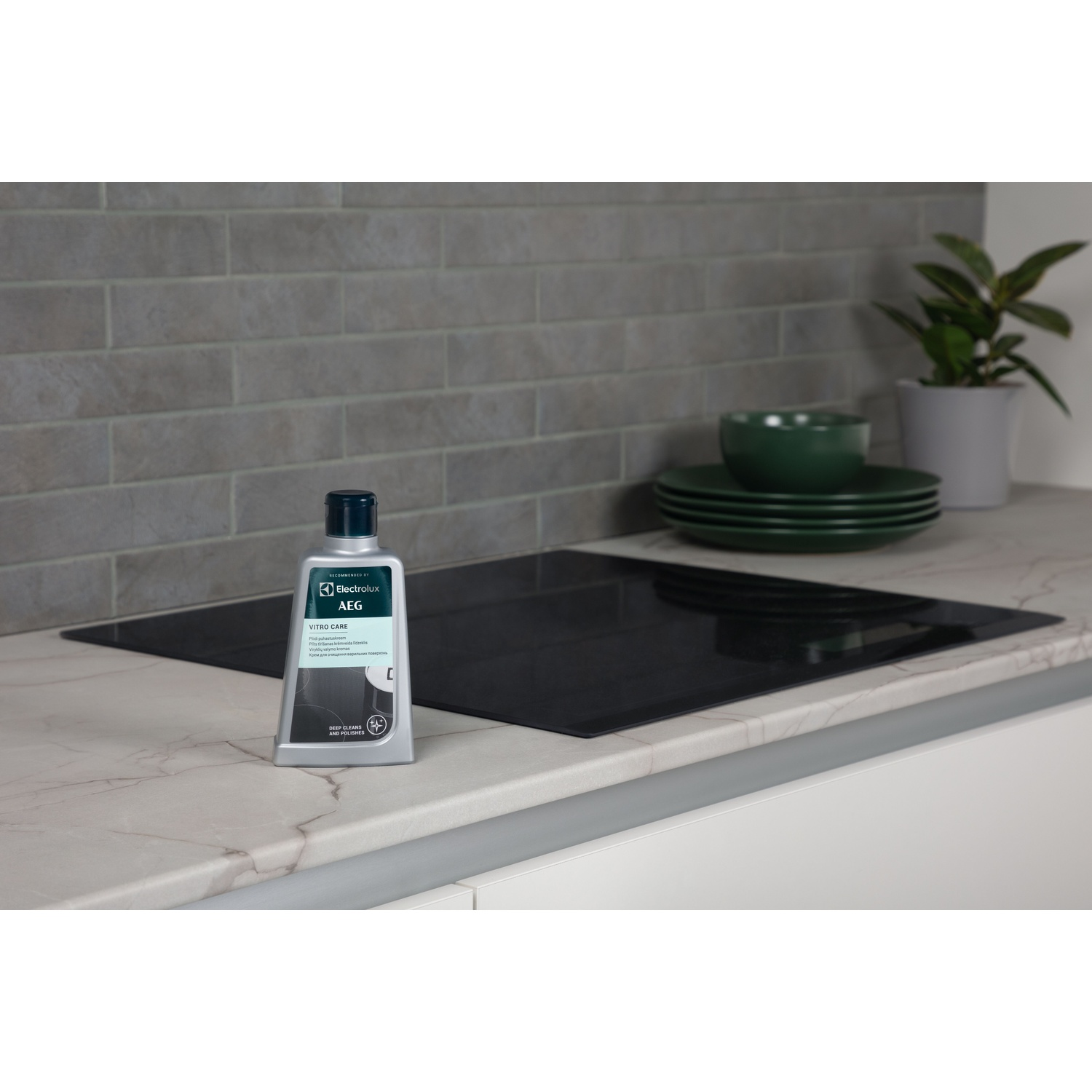 Flacone AEG Vitro Care sul piano cucina. Piano cottura in vetroceramica e piatti verdi visibili.