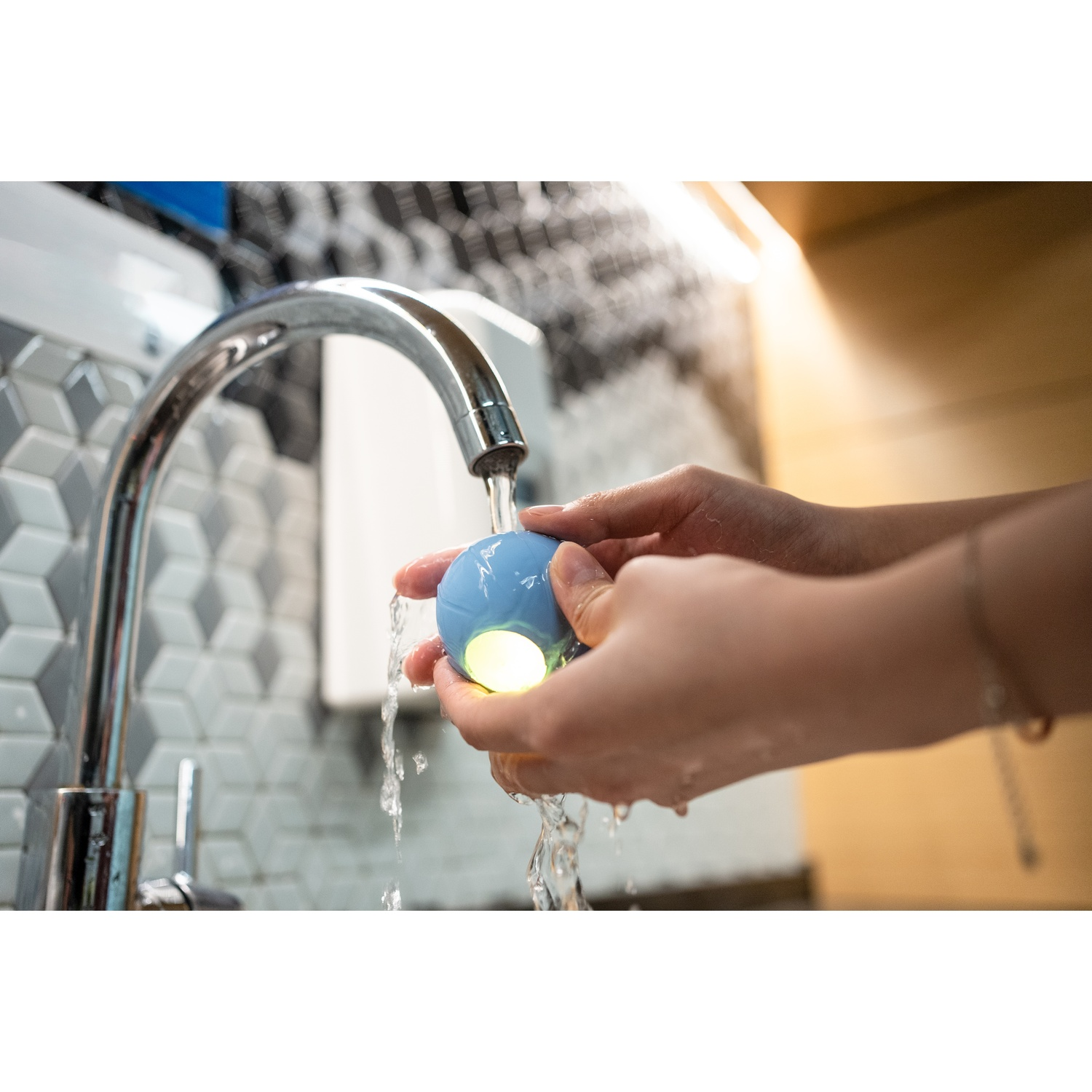 Hands washing with a blue light-up device under a faucet.