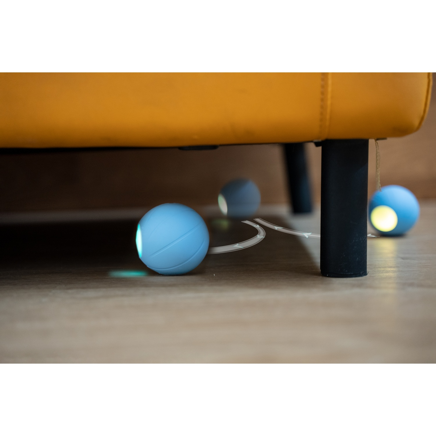 Blue cat toy balls under a yellow couch. The balls have lights inside and a charging line.