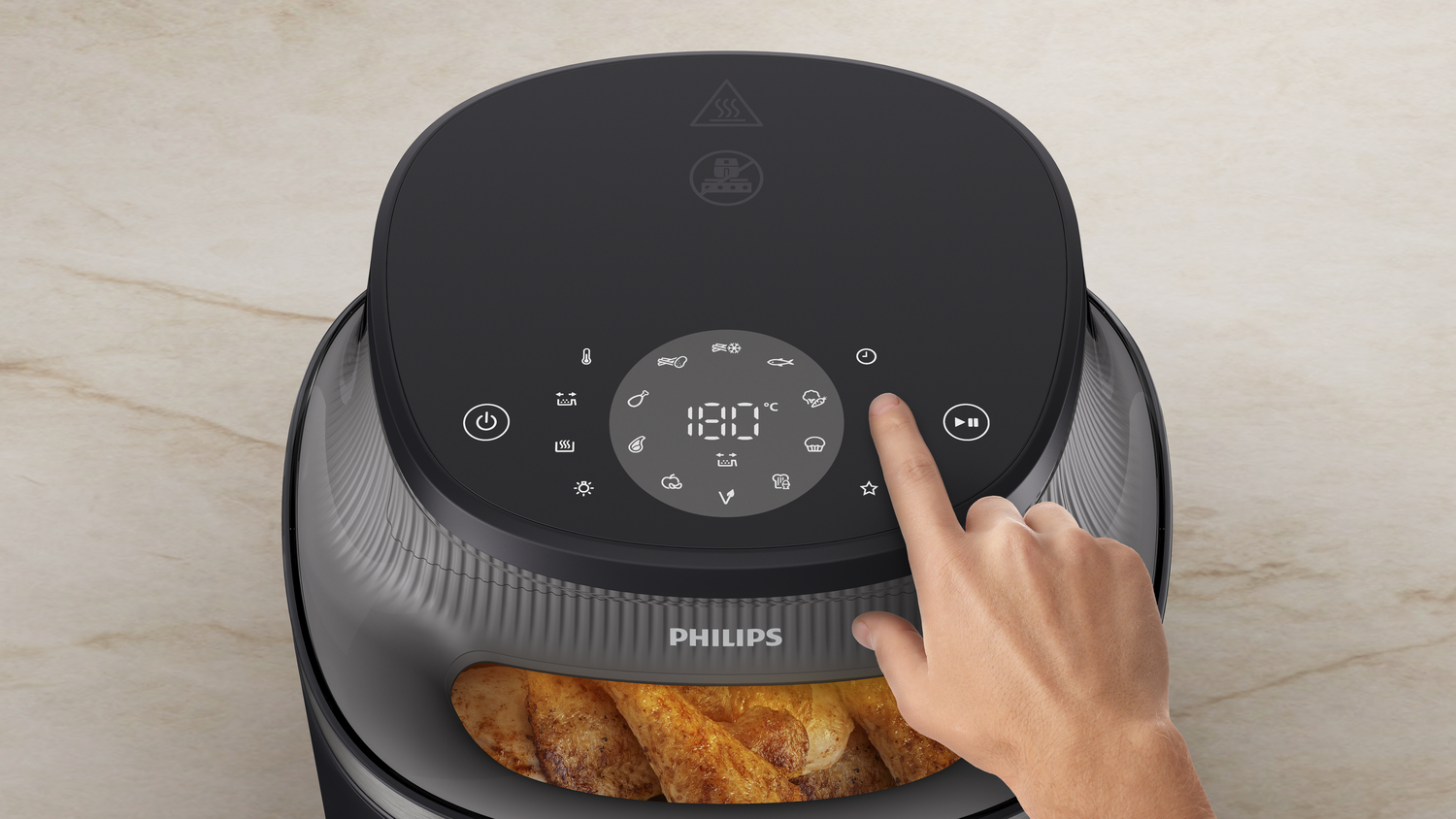 Una mano presiona un botón en una freidora de aire Philips negra. La freidora está en una encimera clara.