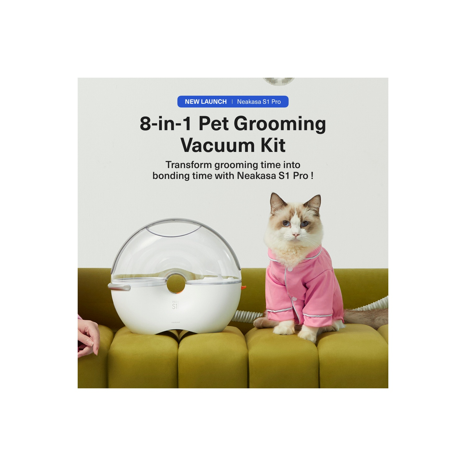 A cat in pink pajamas sits beside a white and clear pet grooming vacuum kit, on a yellow couch.