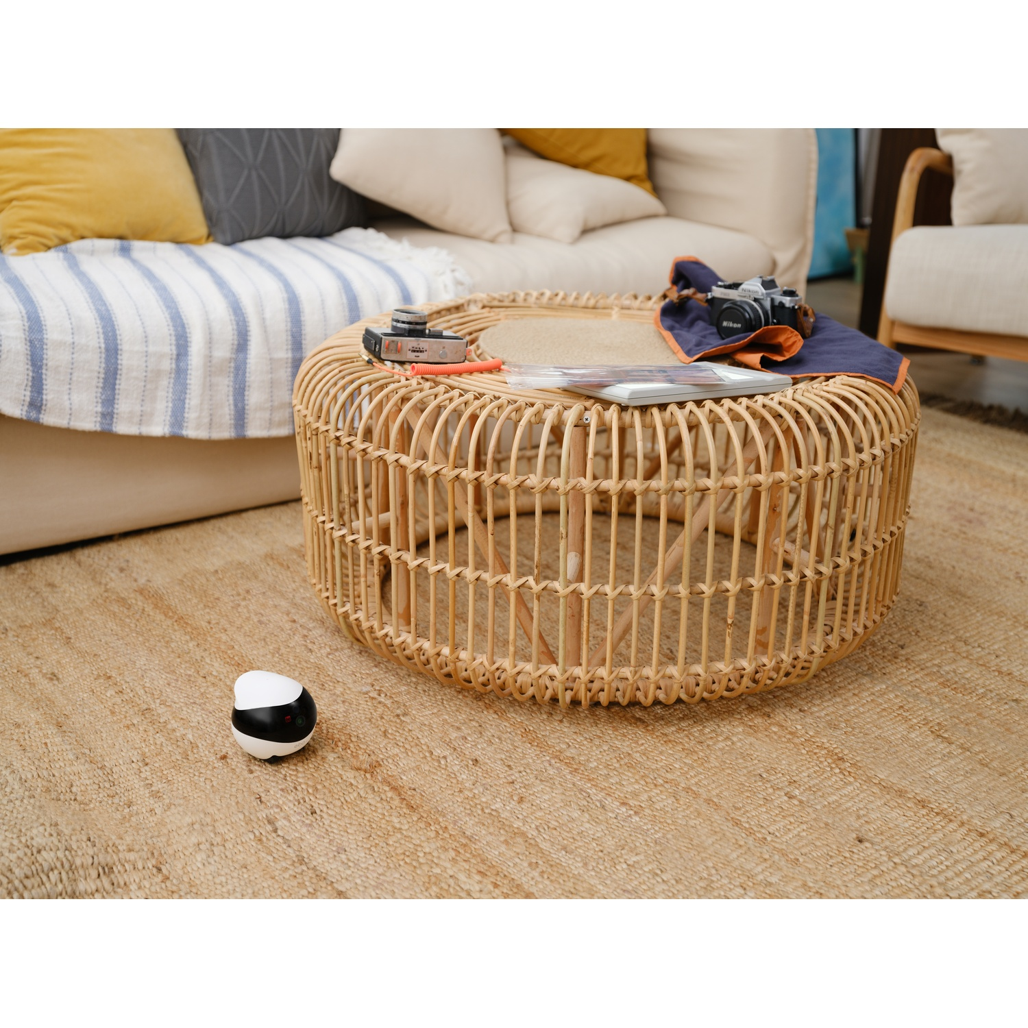 A round, woven coffee table with items on it. A camera and a small robot are visible.