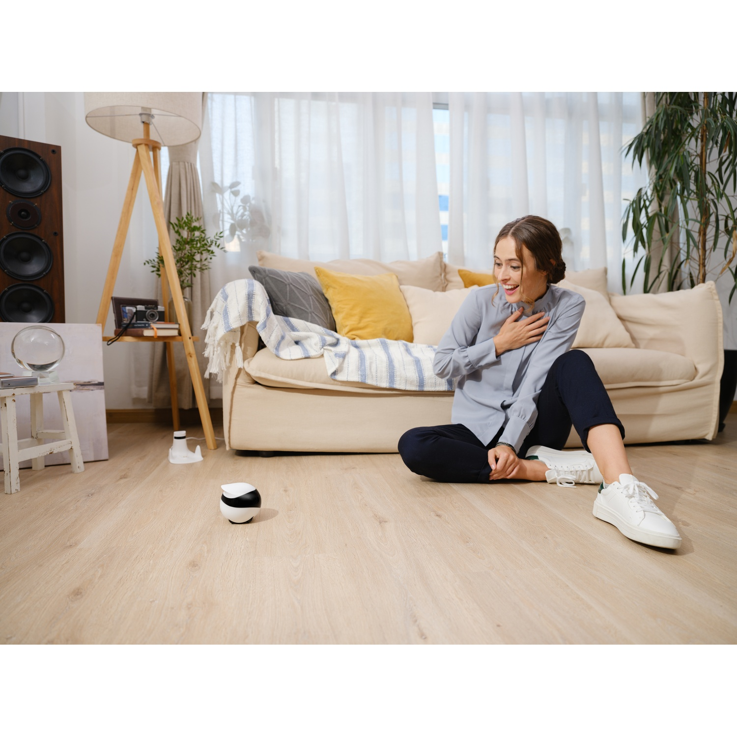 Woman in room, looking at a small, black-and-white device on the floor.