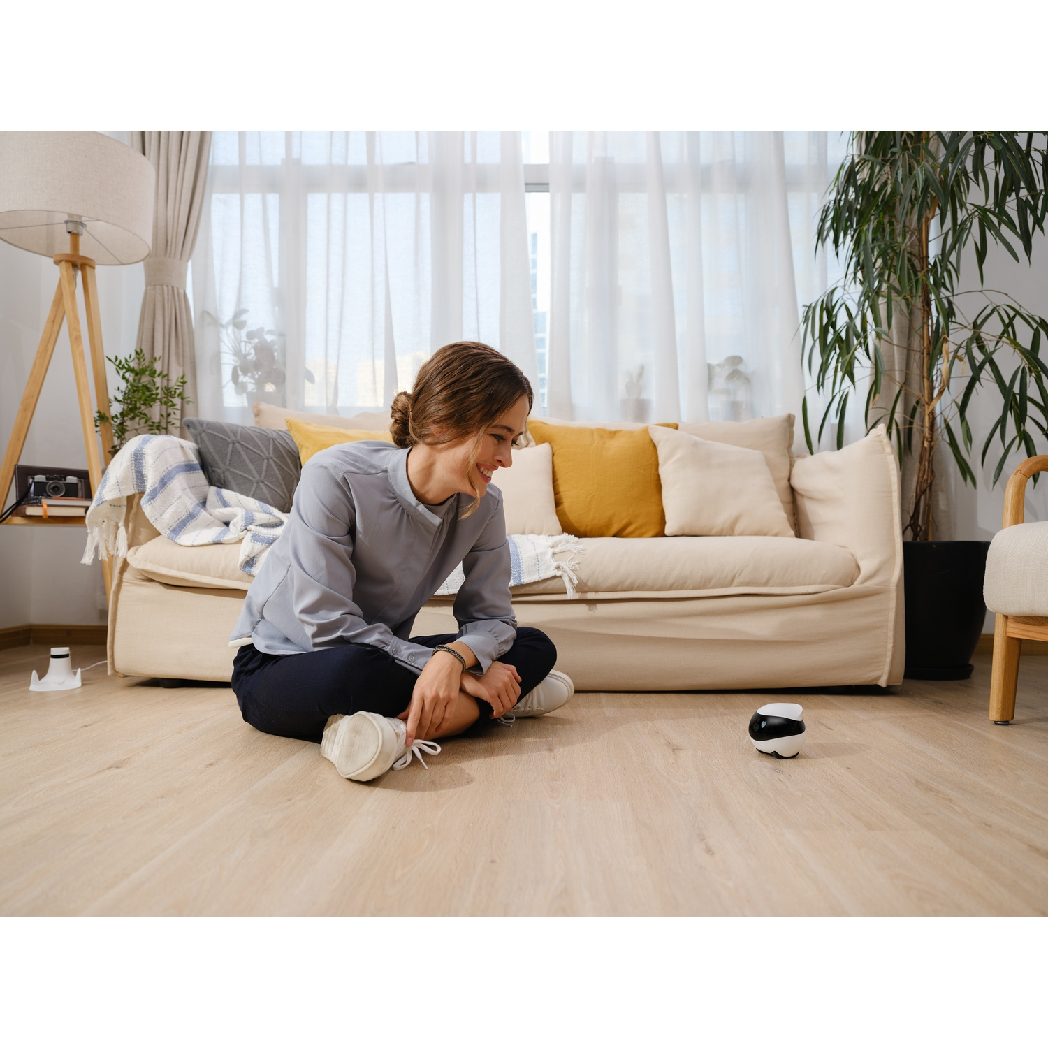 Woman with a robot toy, sitting on a wooden floor, with a sofa in background.