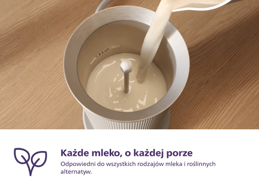 Mleko wlewa się do spieniacza. Spieniacz jest biały, na jasnej drewnianej powierzchni.