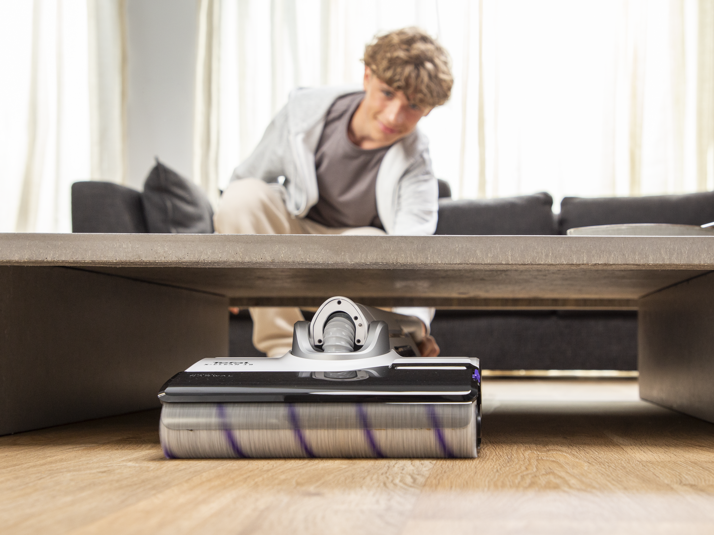 Osoba odkurza odkurzaczem. Głowica odkurzacza jest na pierwszym planie.