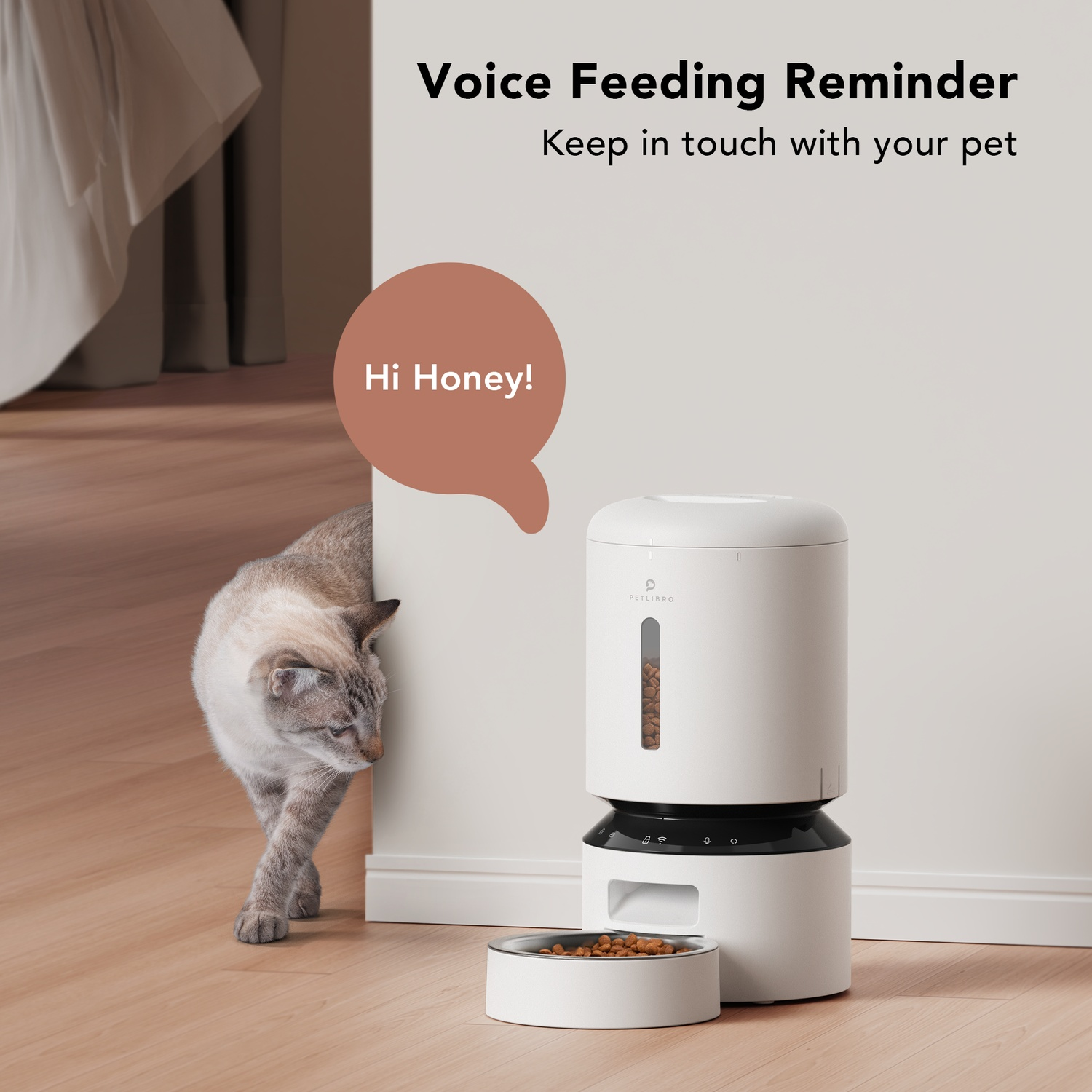A white automatic pet feeder with a cat peeking from behind a wall. A speech bubble says, "Hi Honey!"