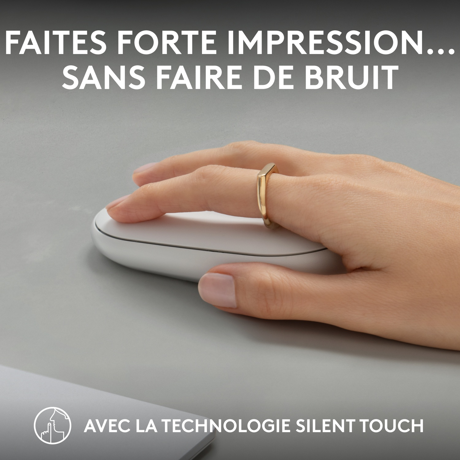 Main avec une bague en or utilisant une souris blanche sur une surface grise.