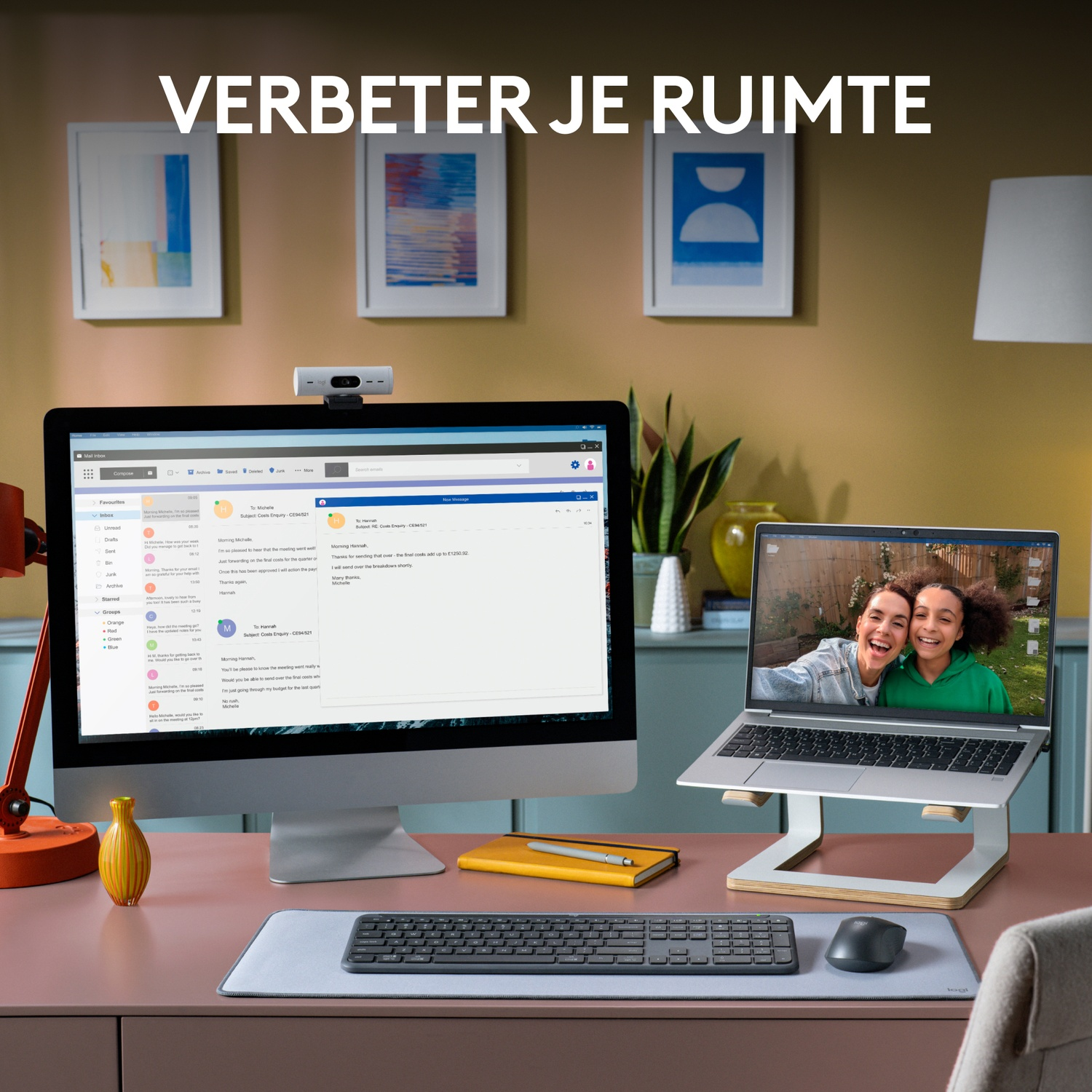 Desk setup with monitor, laptop, webcam, keyboard, mouse, and yellow notepad.