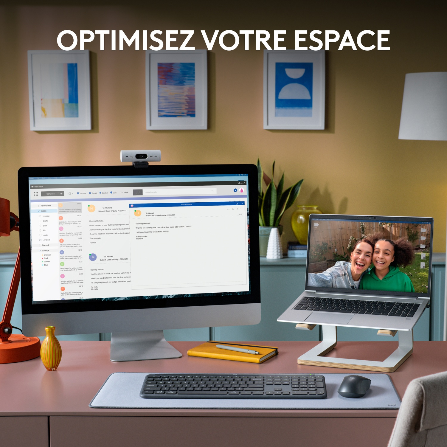 Une configuration de bureau avec un moniteur, un ordinateur portable, un clavier et une webcam ; deux femmes sur l'écran de l'ordinateur portable.