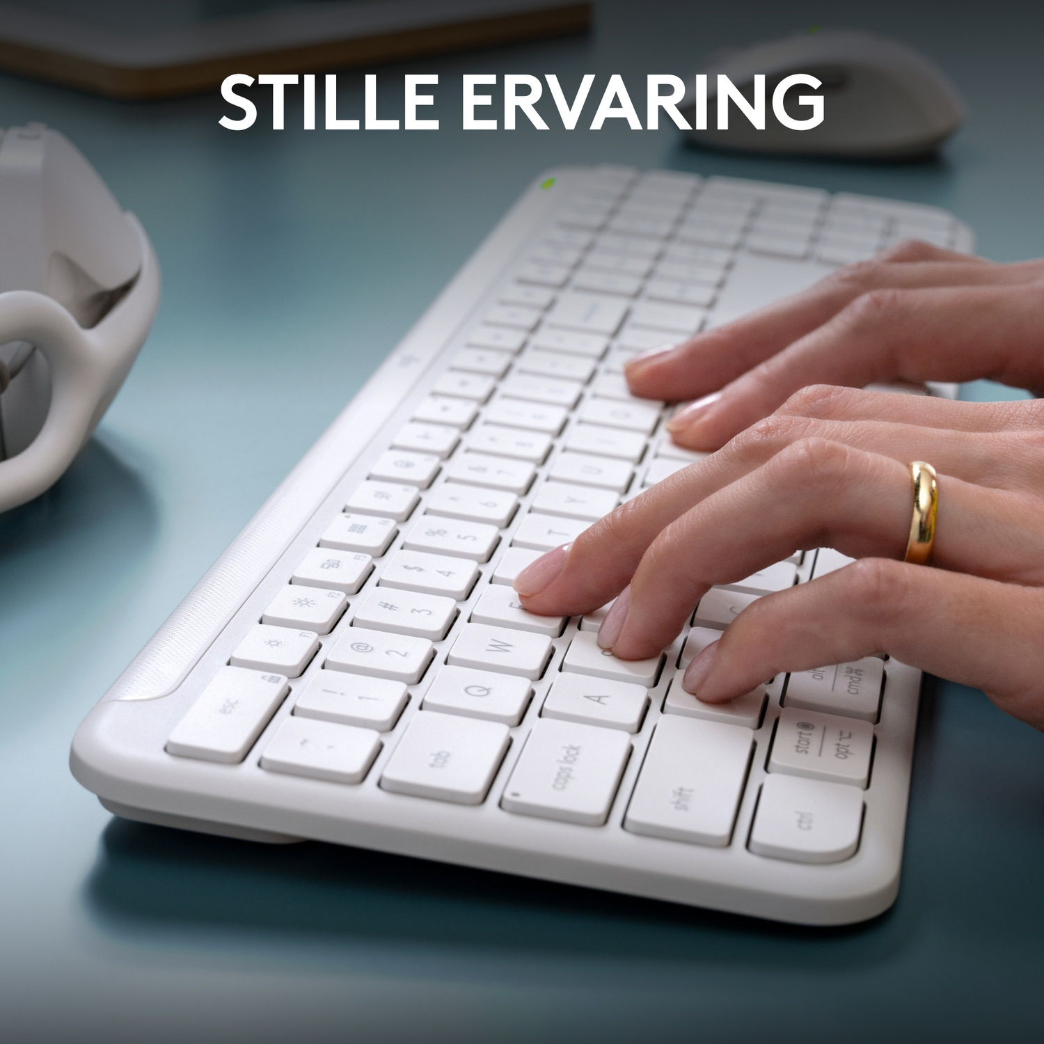 Hands typing on a white keyboard. Gold ring is visible. The background is blurred.