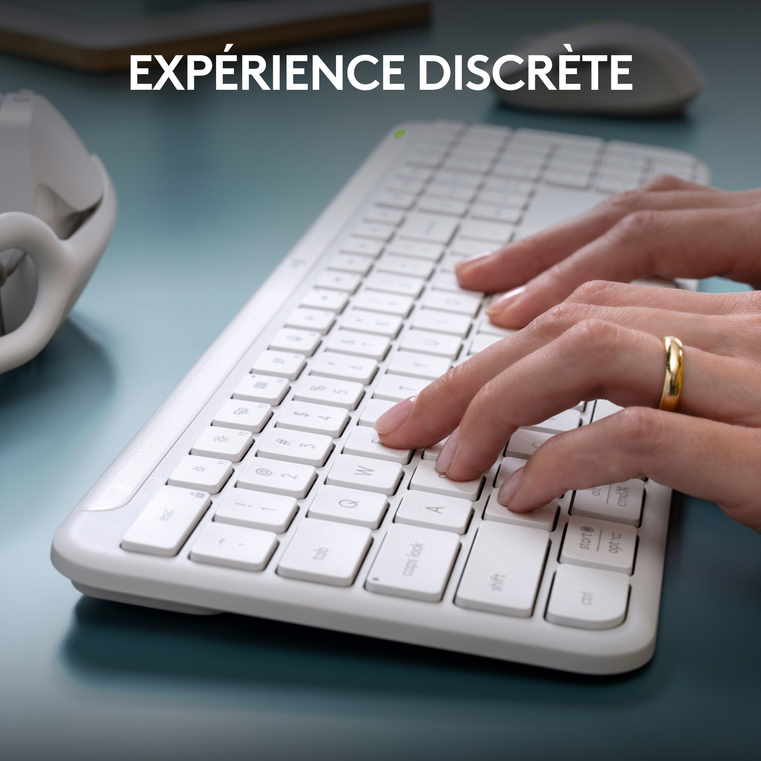 Mains tapant sur un clavier blanc avec une bague au doigt. Le fond est un bureau bleu.