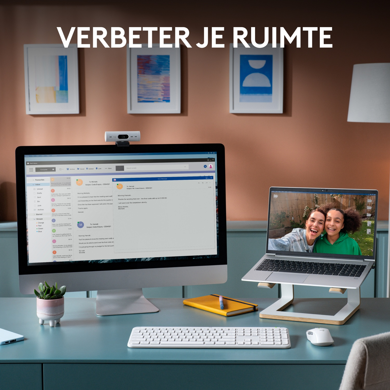 Desk with a computer, monitor, laptop, keyboard, mouse, and webcam. Two women are on the laptop screen.