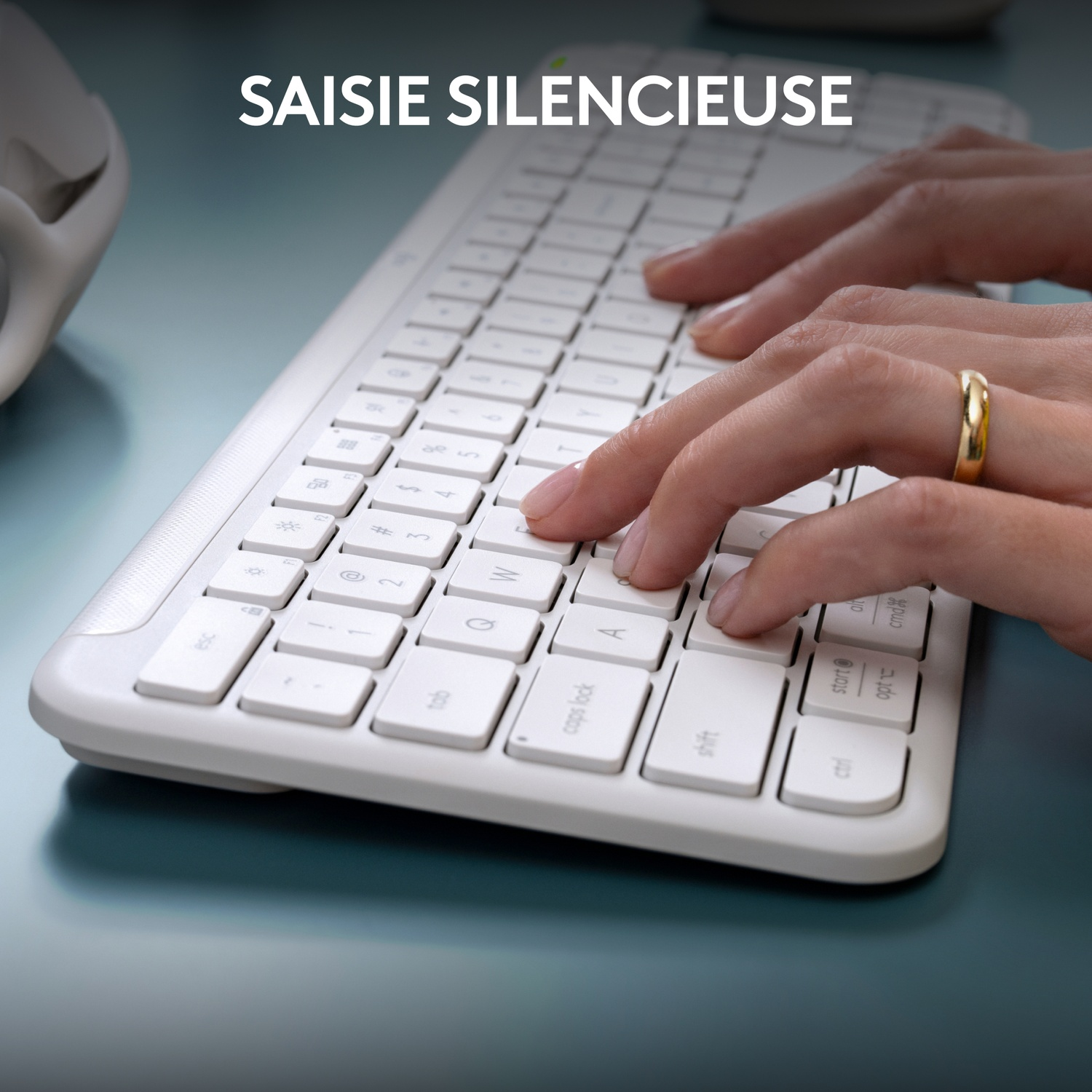 Mains tapant sur un clavier blanc avec une bague dorée au doigt.