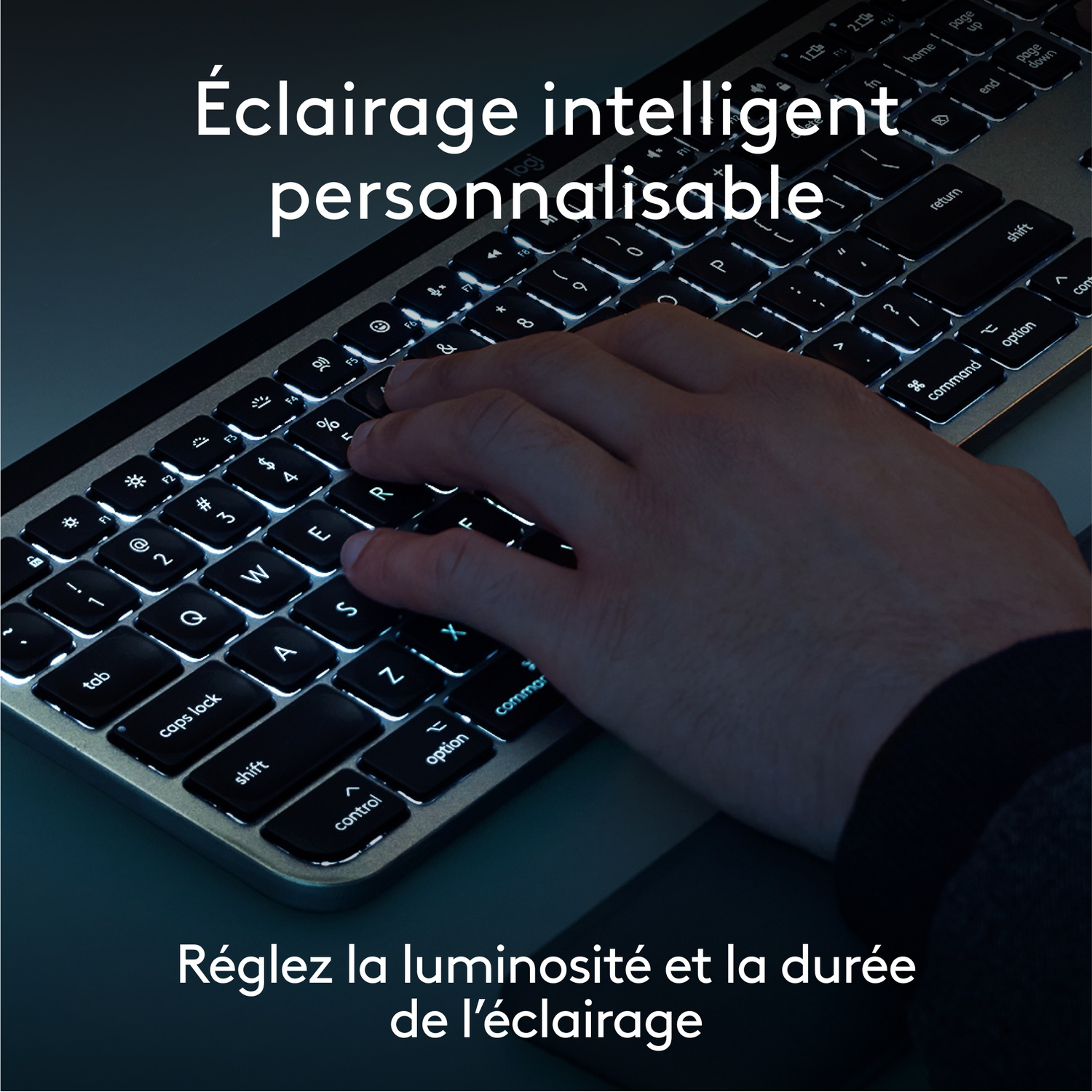 Une main tape sur un clavier rétroéclairé avec des touches blanches et un cadre argenté.